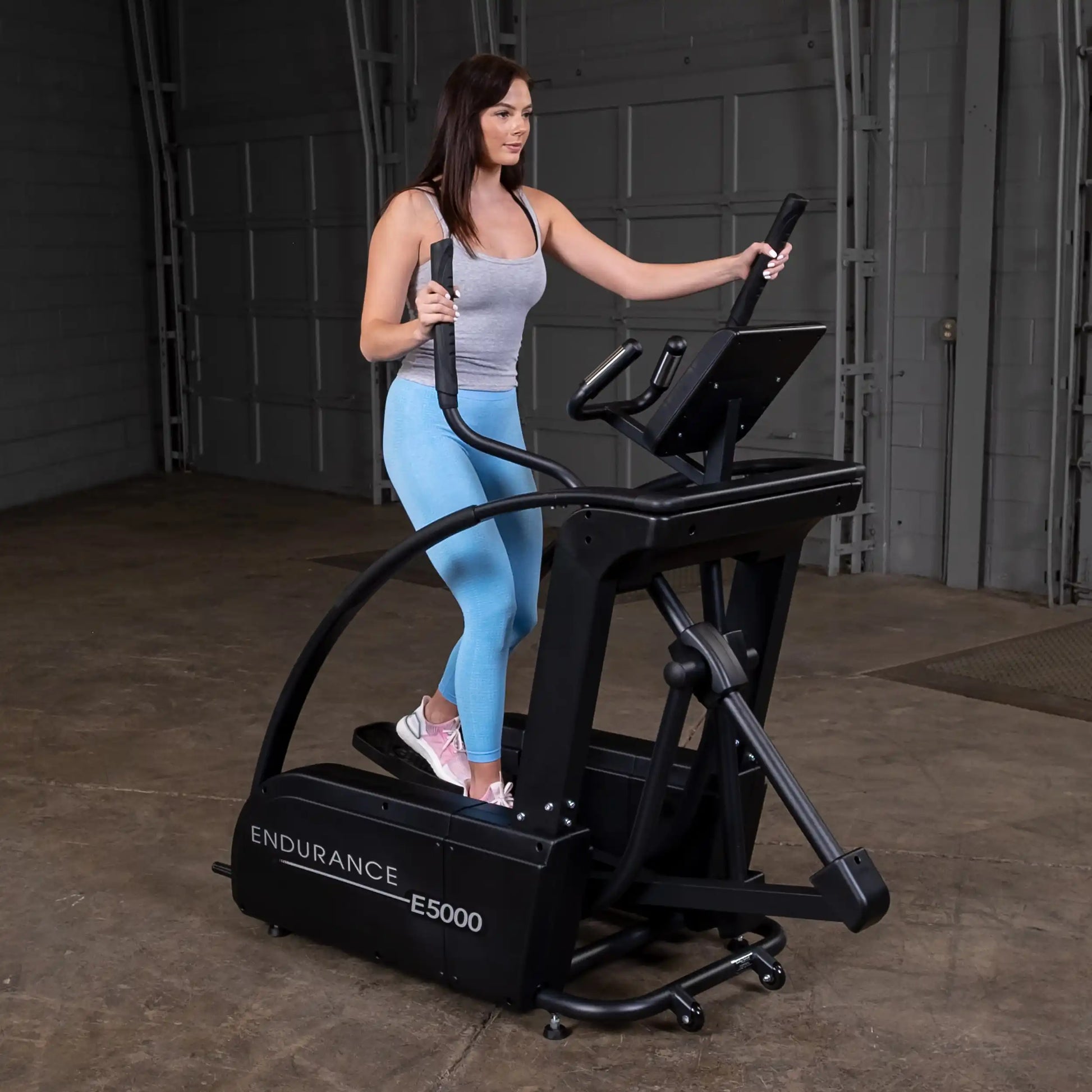 Woman using Endurance E5000 elliptical in a gym, wearing blue leggings and pink sneakers.