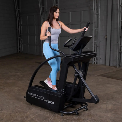 Woman using Endurance E5000 elliptical in a gym, wearing blue leggings and pink sneakers.