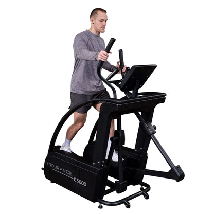 Man exercising on Endurance E5000 elliptical machine, wearing gray shirt and shorts.