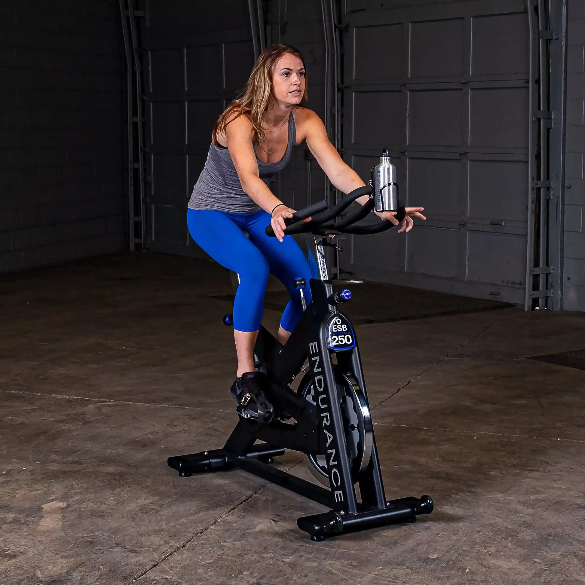 Woman exercising on Endurance ESB250 indoor cycling bike in a garage.