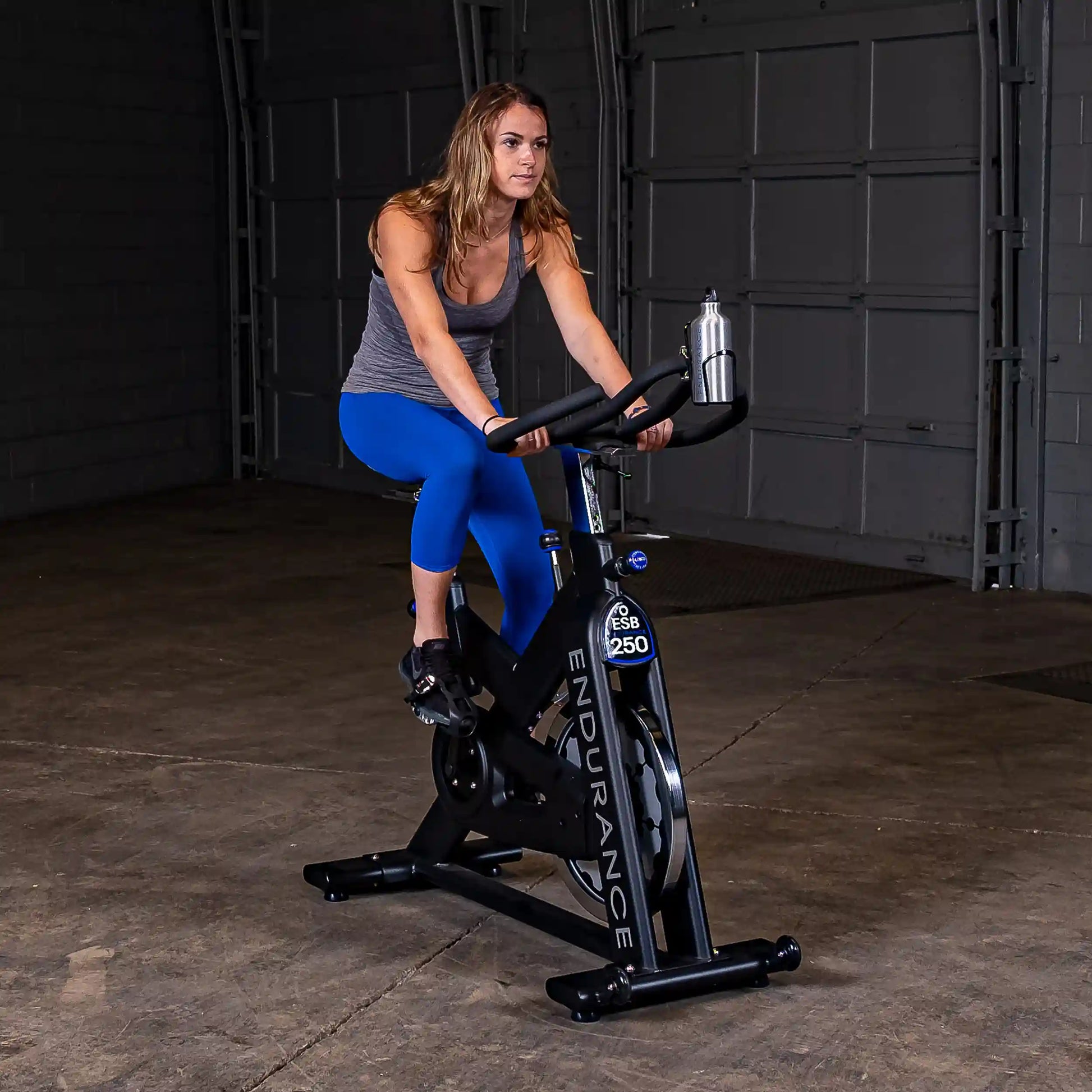 Woman exercising on Endurance ESB250 indoor cycling bike in a garage.