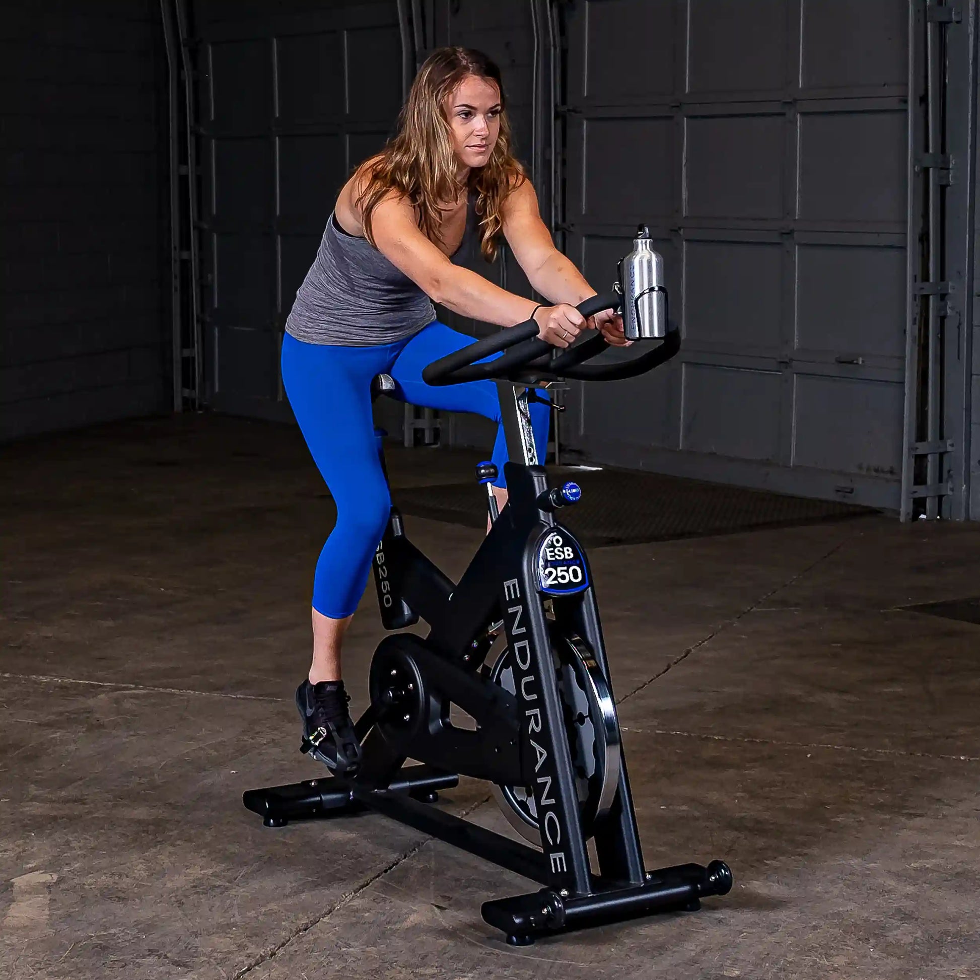Woman exercising on Endurance ESB250 bike, wearing blue leggings in a garage setting.