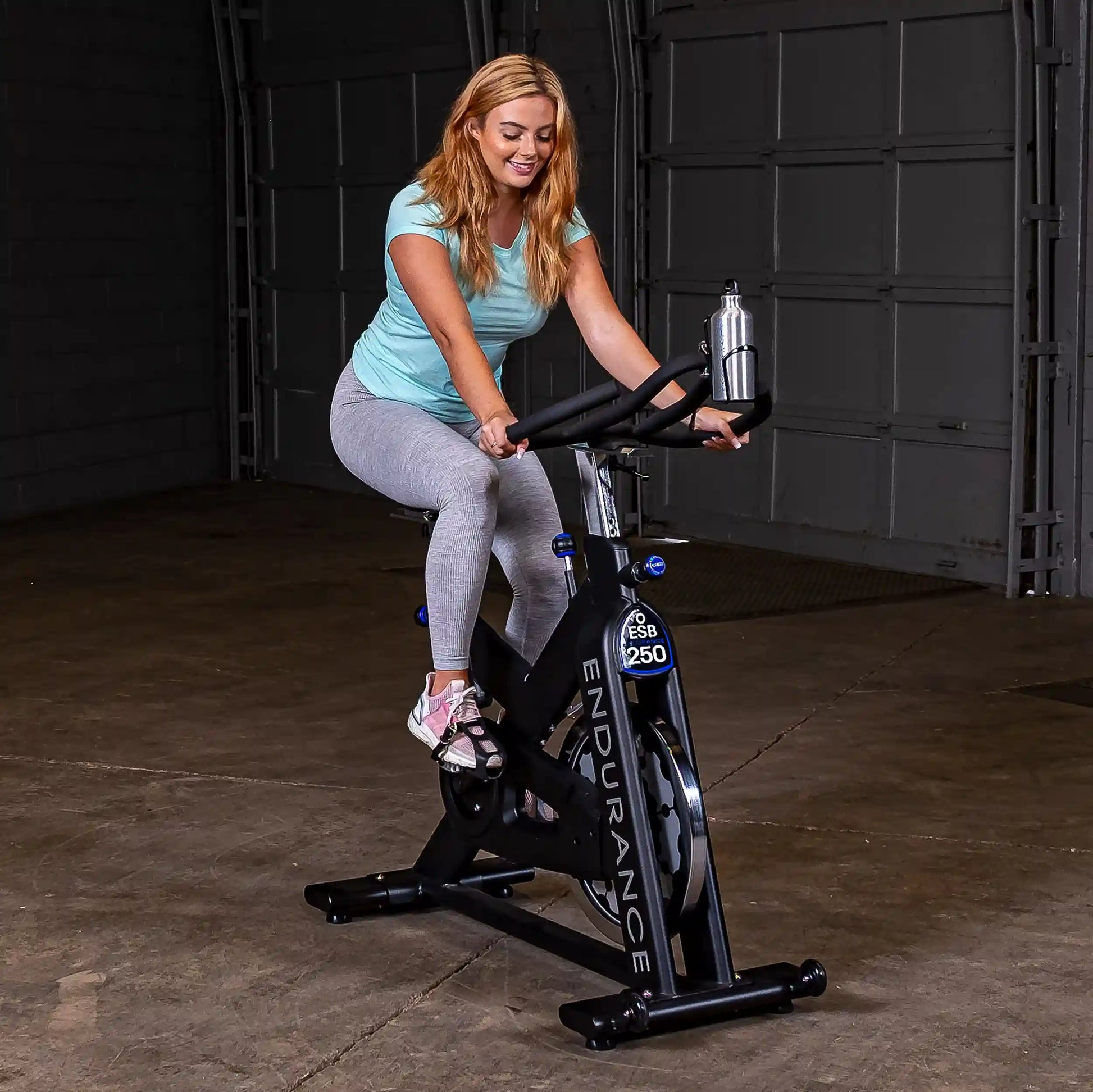 Woman exercising on Endurance ESB250 indoor cycling bike in a garage.