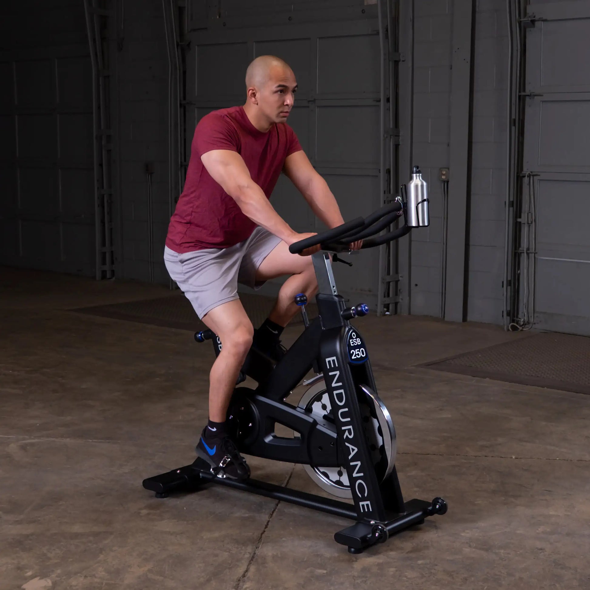 Man in red shirt using Endurance ESB250 stationary bike in a garage.