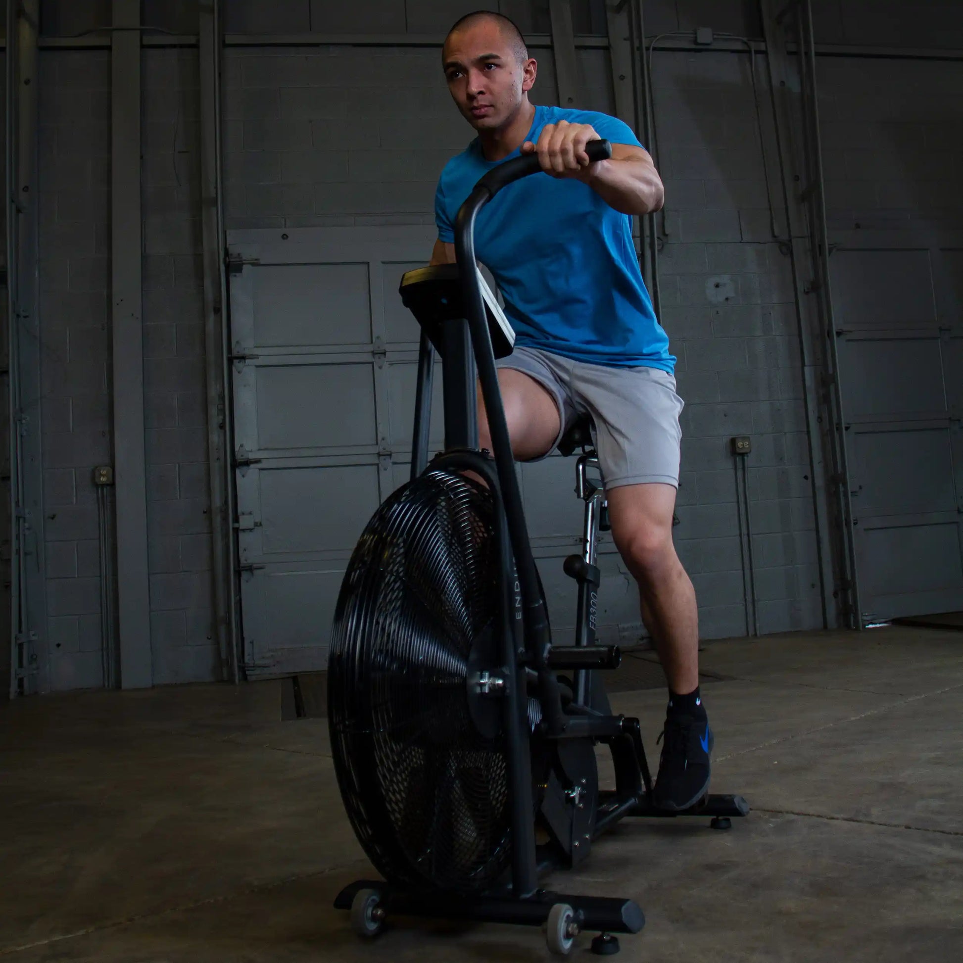 Man in blue shirt using a stationary air bike in a gym.