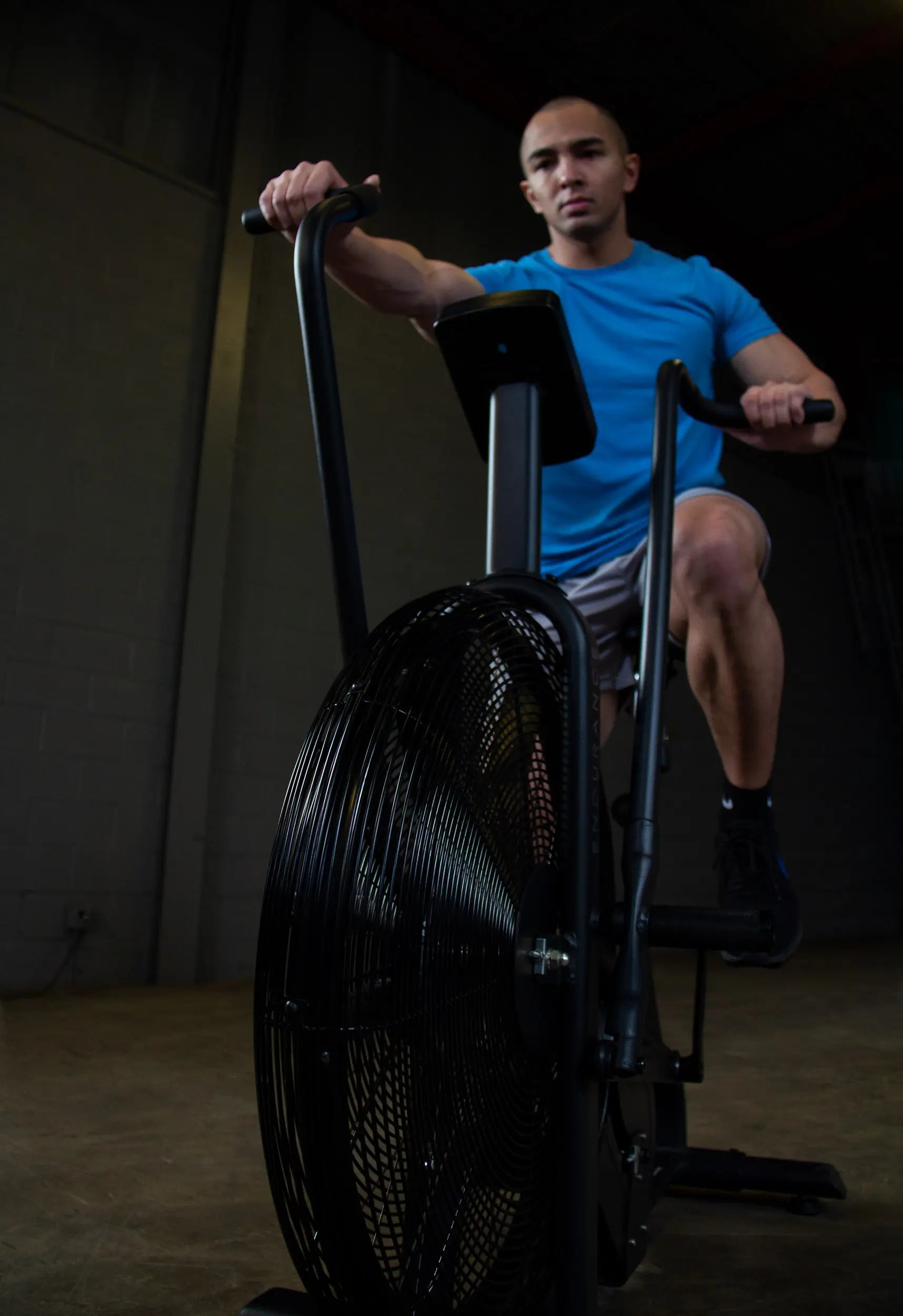Man exercising on black assault bike in a gym, wearing a blue shirt.