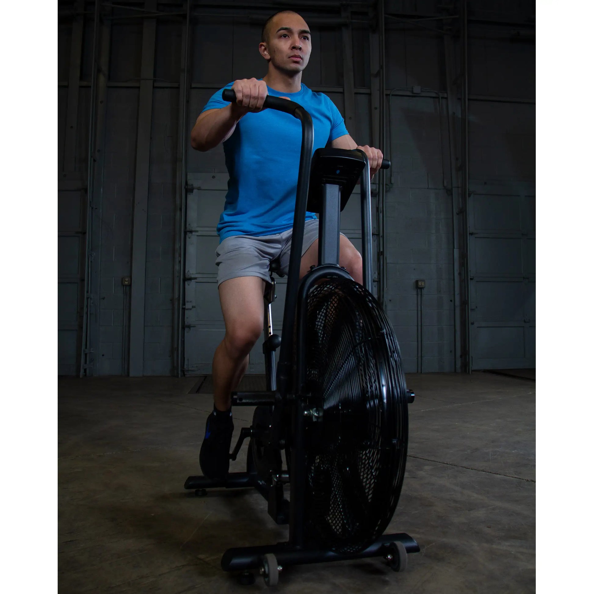 Man exercising on black air bike in warehouse gym.