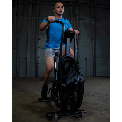 Man exercising on black air bike in warehouse gym.