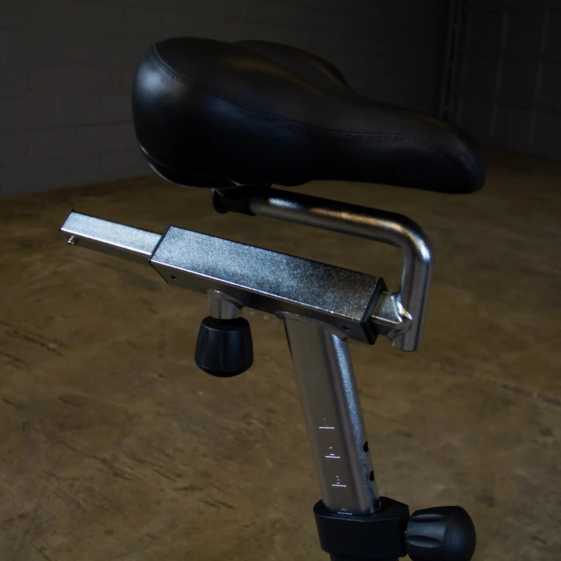 Adjustable black leather bike seat with a silver frame in an indoor setting.