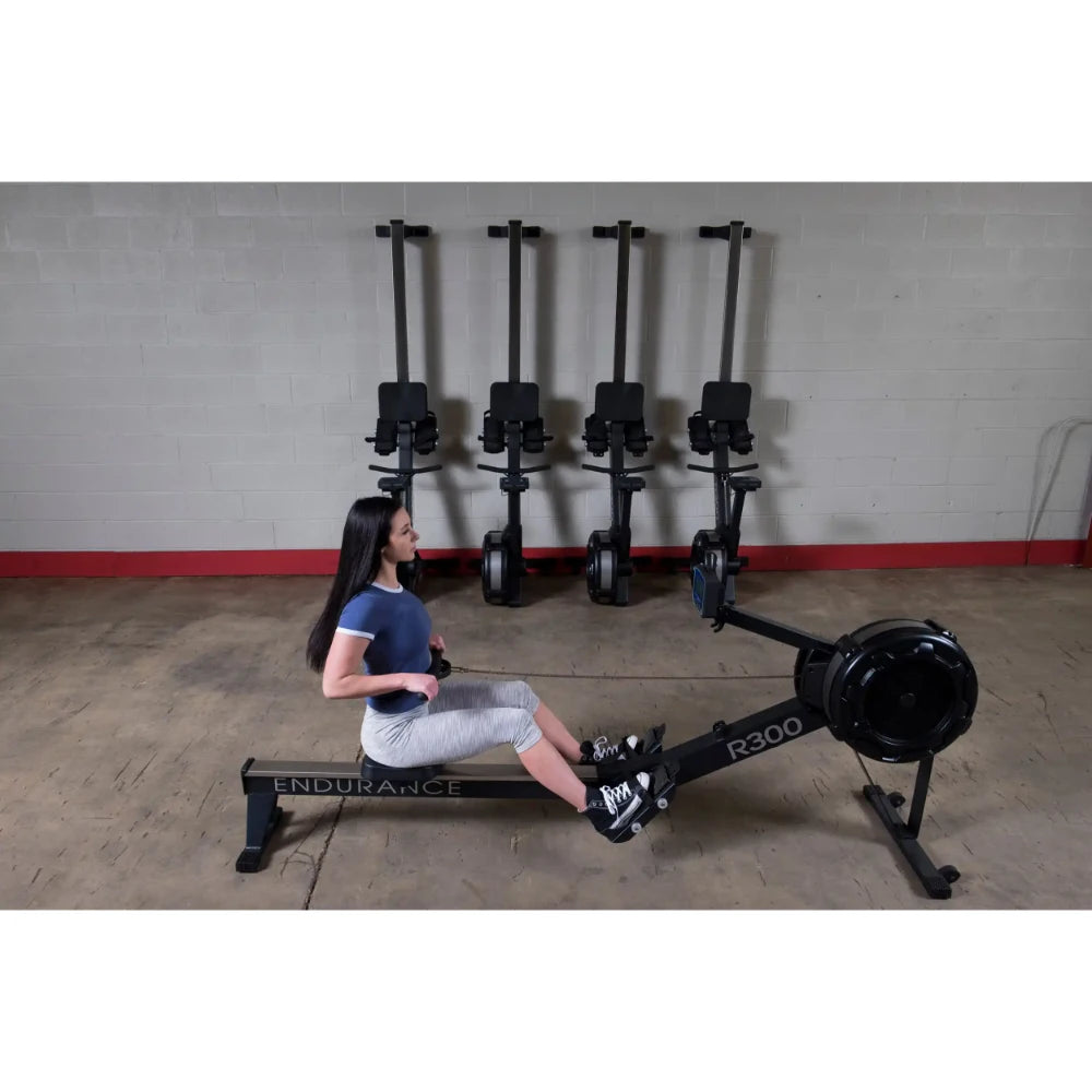 Woman using Endurance R300 rowing machine in a gym with four rowers on the wall.