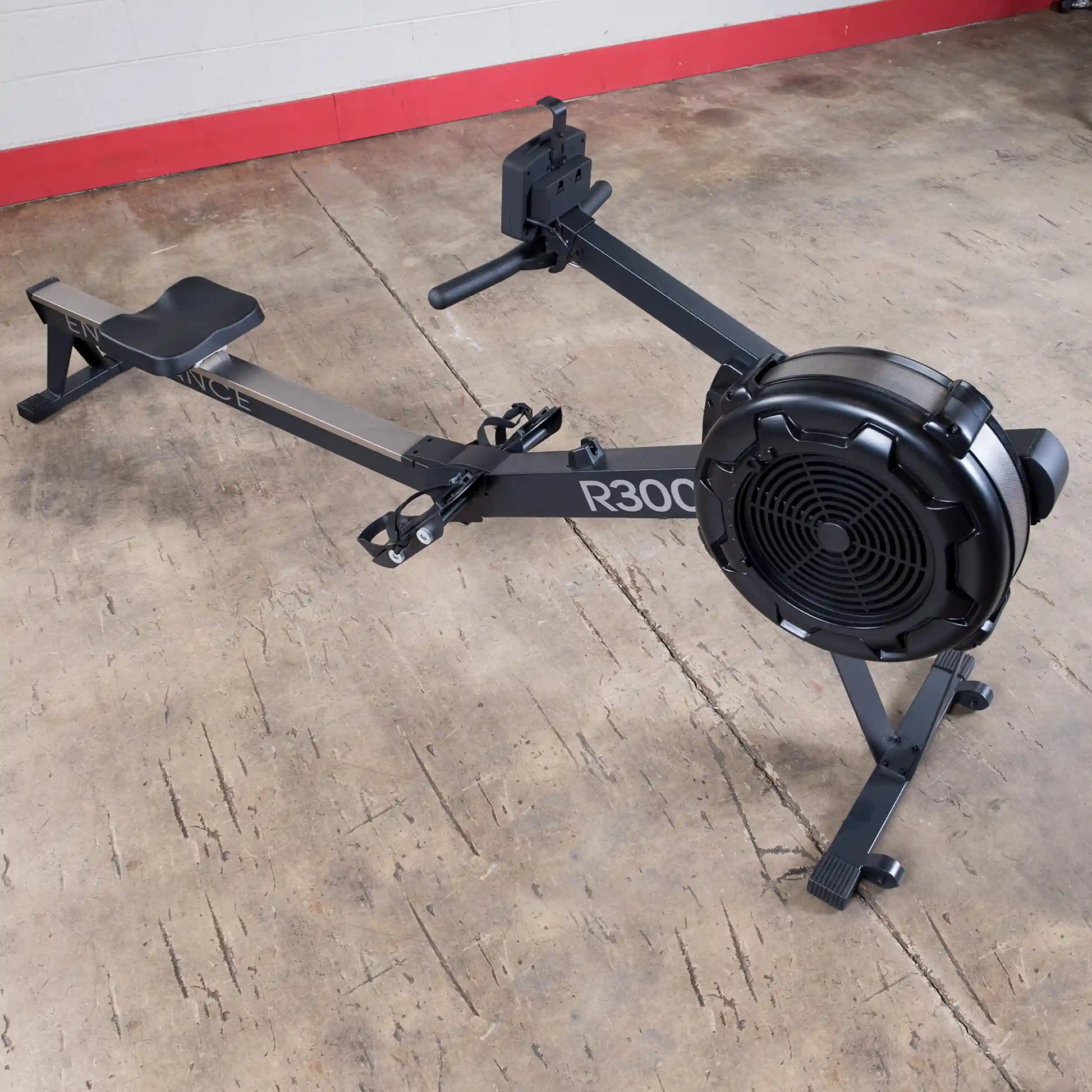 R300 rowing machine with black fan and seat on concrete floor.