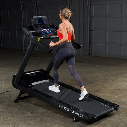 Woman running on Endurance treadmill in a garage, wearing a red top and black leggings.
