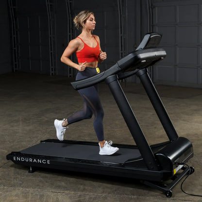 Woman running on Endurance treadmill in a red top and black leggings.