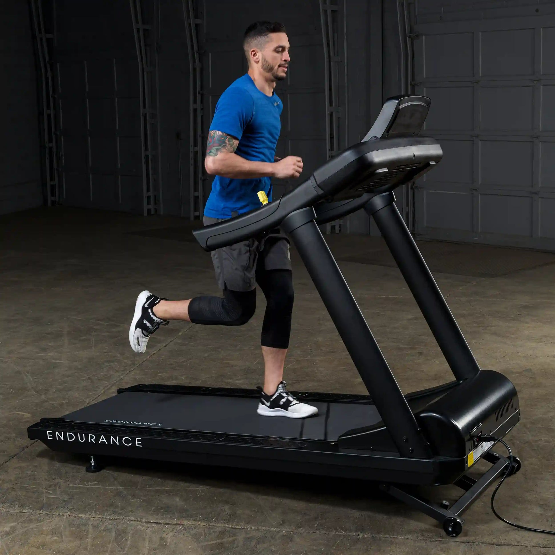 Man jogging on black Endurance treadmill in a dimly lit room.