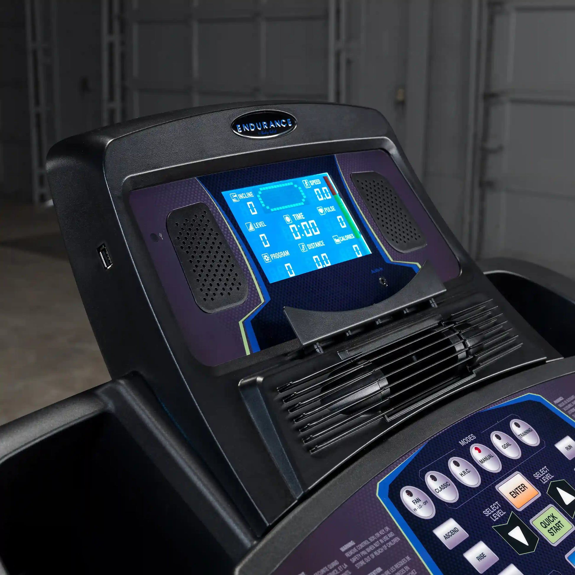 Endurance treadmill console with blue digital display and control buttons in a dark gym setting.