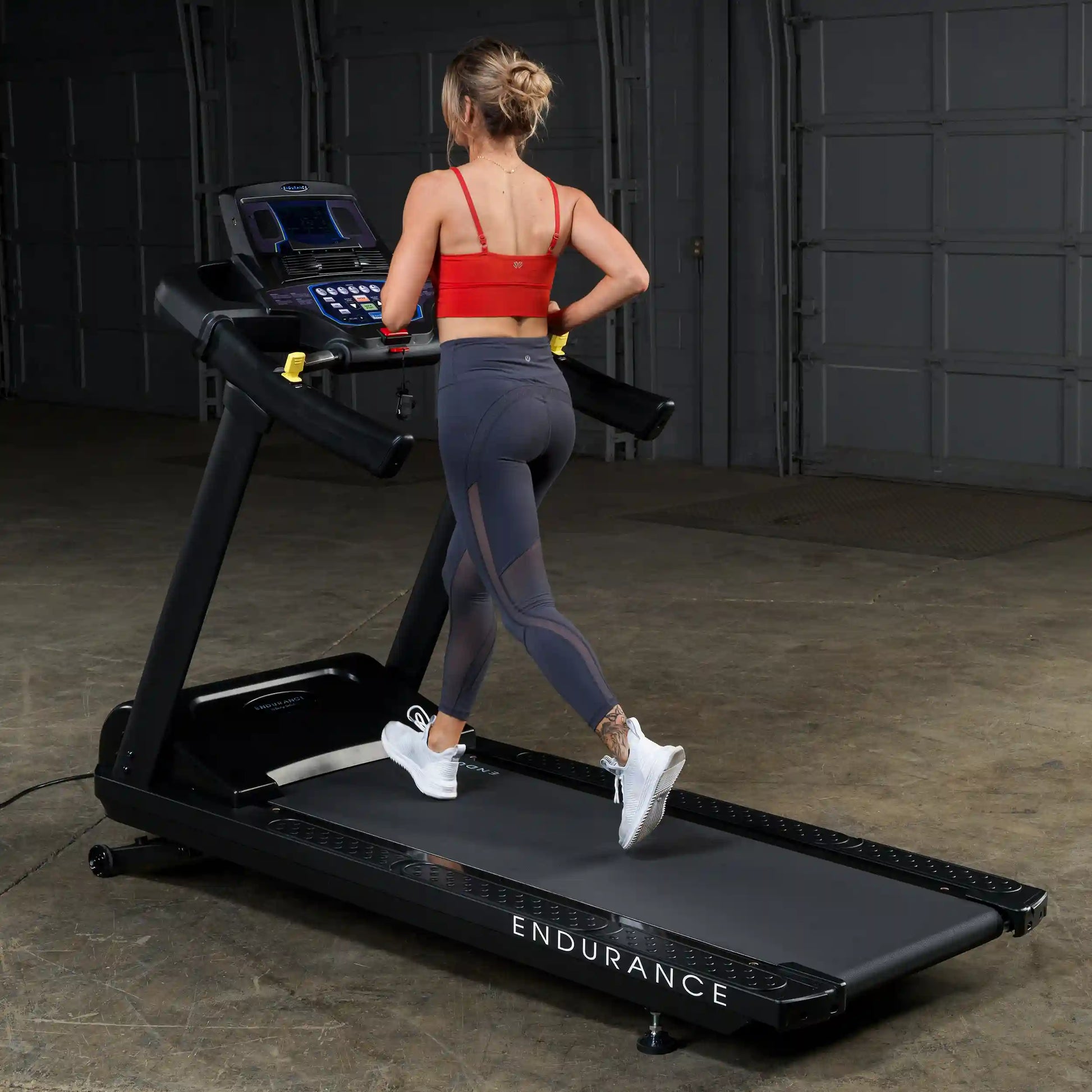 Woman running on Endurance treadmill in red sports bra and gray leggings.