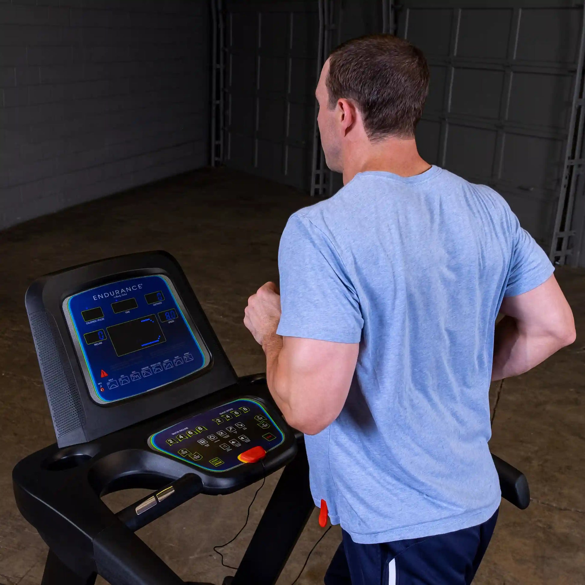 Man running on Endurance treadmill in a garage, wearing a light blue shirt.