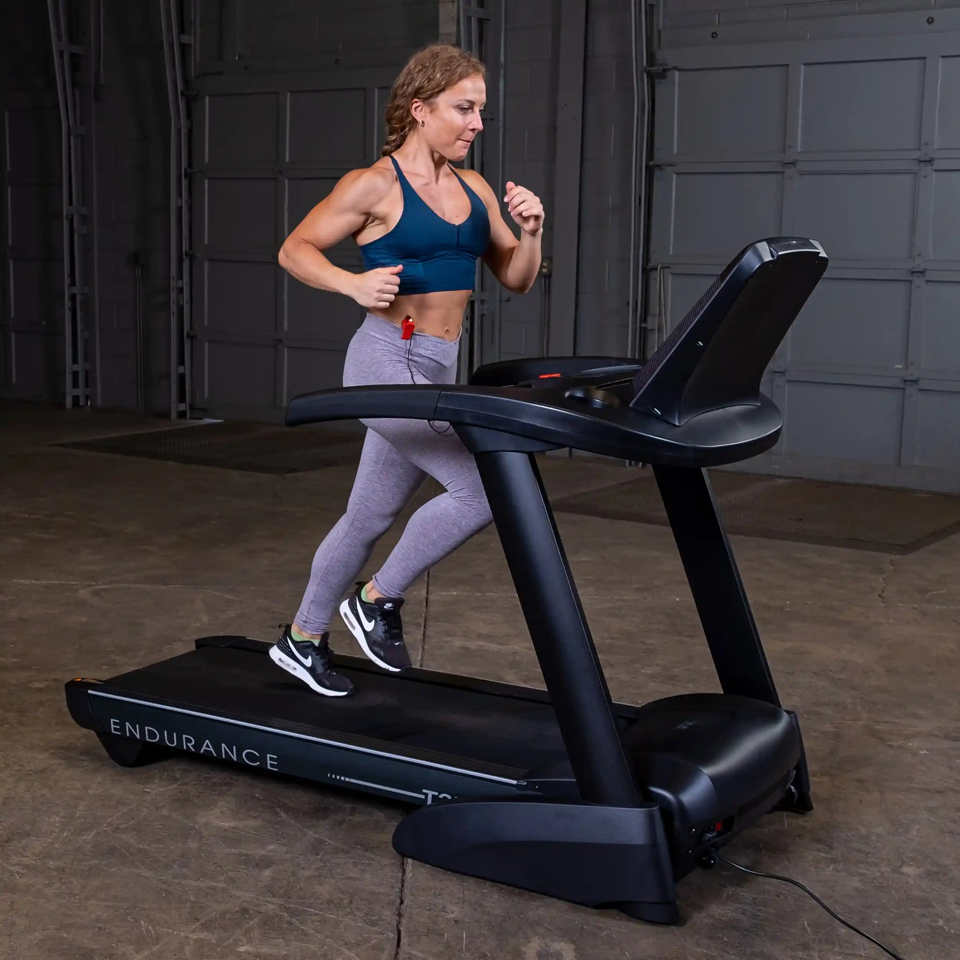 Woman running on Endurance treadmill in gray leggings and blue sports bra.