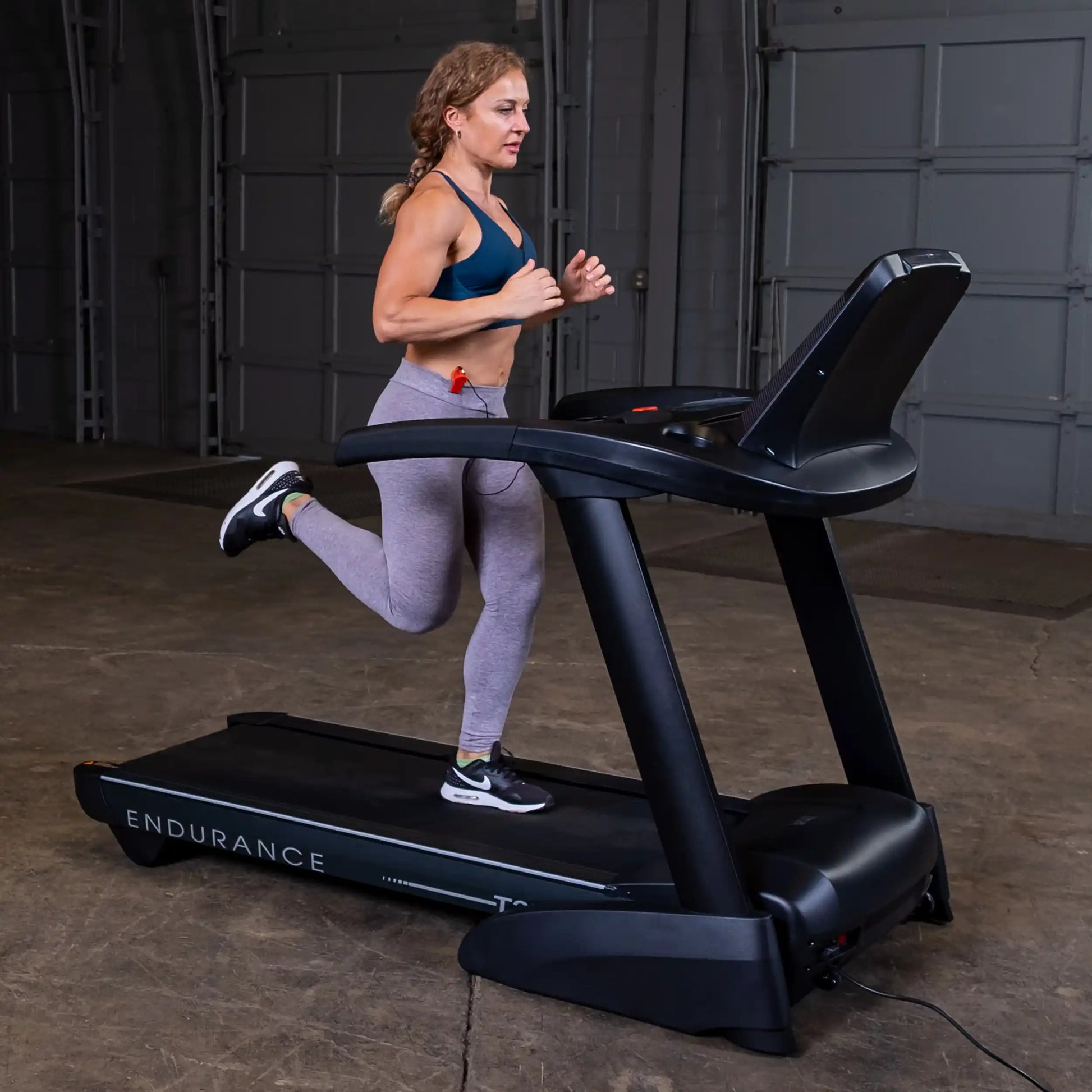 Woman running on Endurance treadmill in gray leggings.
