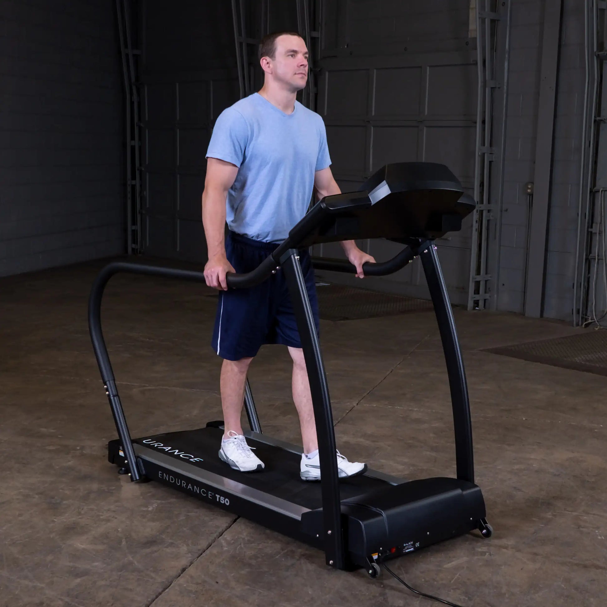 Man walking on Endurance T50 treadmill in a gym, wearing blue shirt and navy shorts.