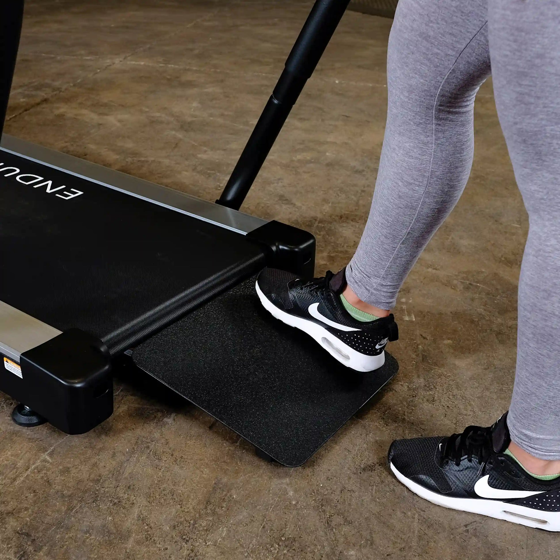 Person stepping onto Endurance treadmill with black Nike shoes, highlighting fitness equipment use.