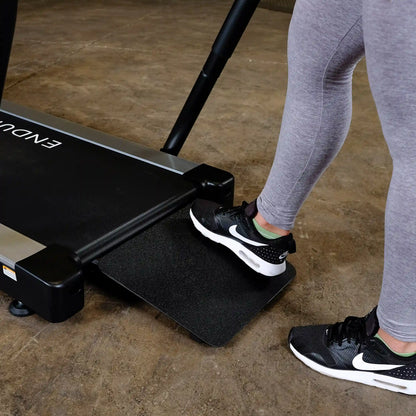 Person stepping onto Endurance treadmill with black Nike shoes, highlighting fitness equipment use.