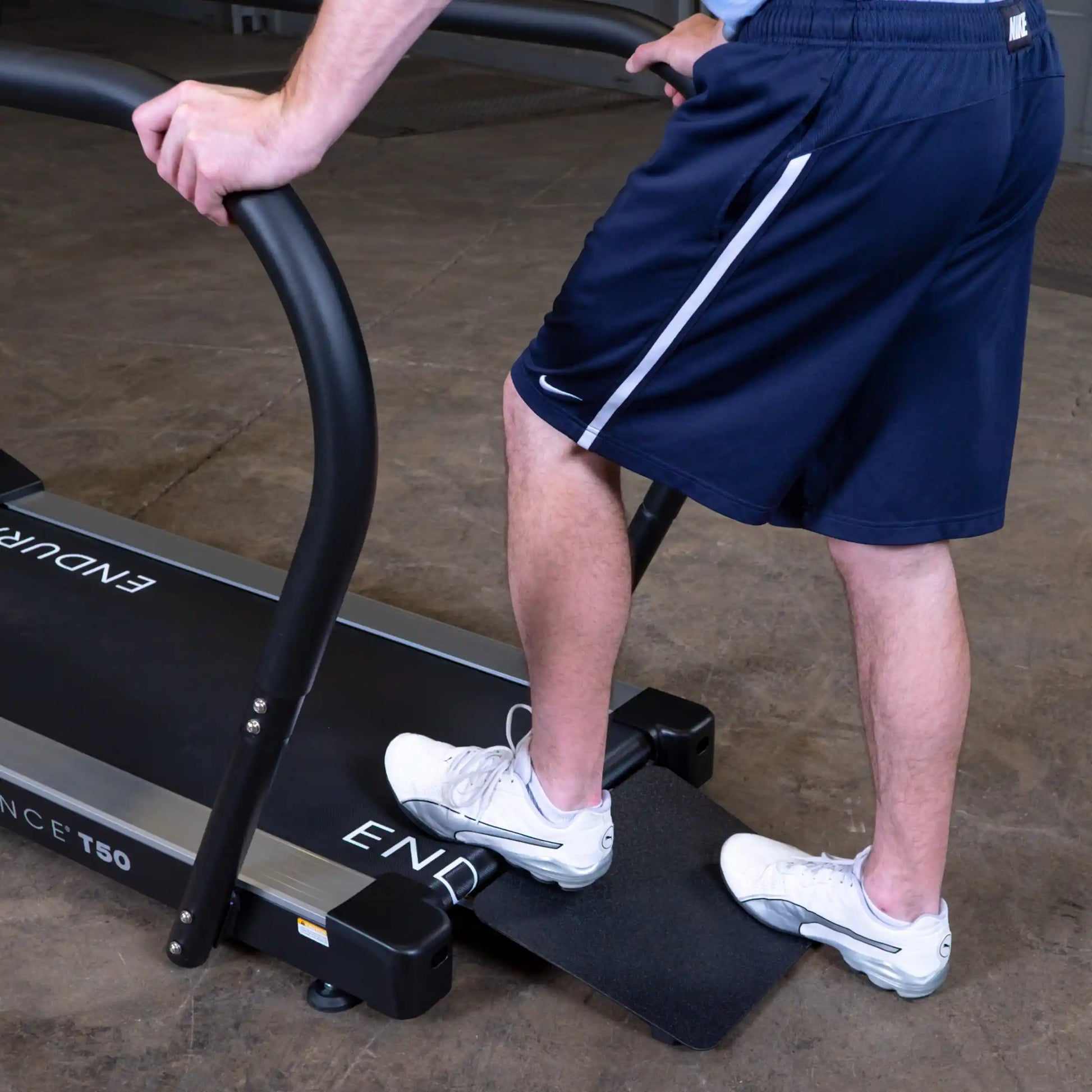 Person using Endurance T50 treadmill with black handrails in a gym setting.