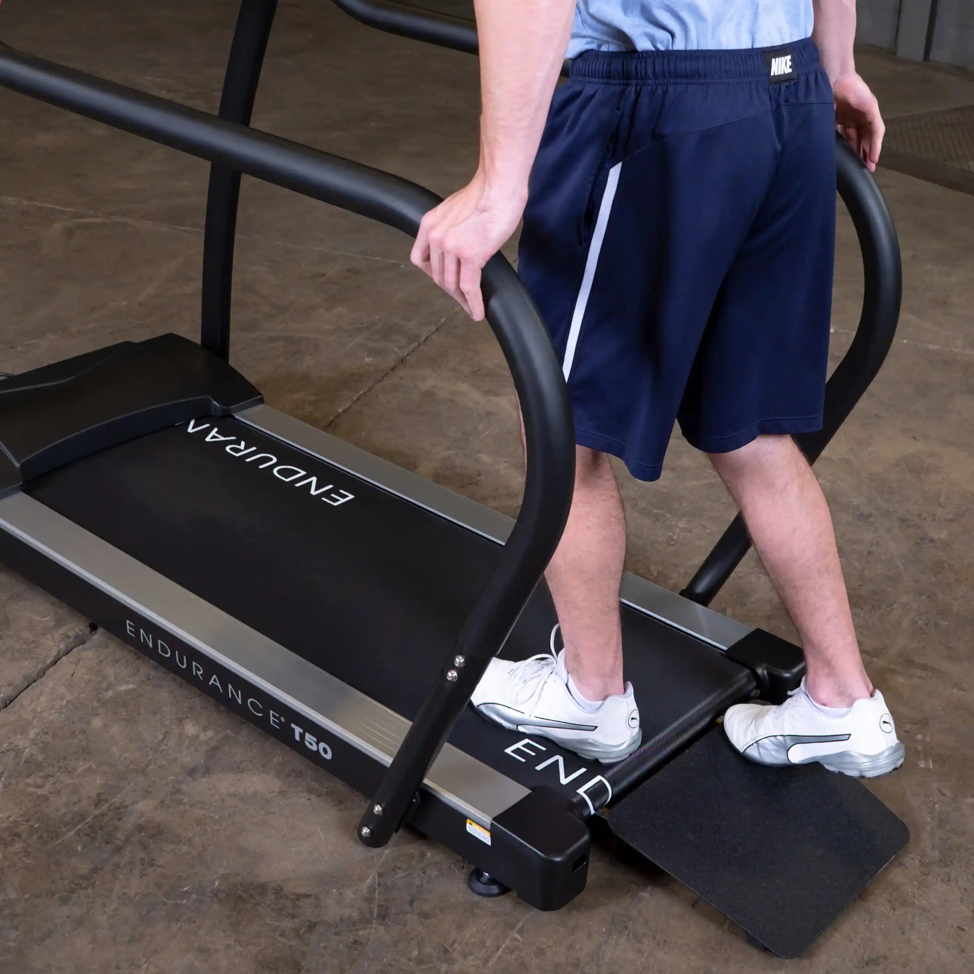 Man in Nike shorts using Endurance T50 treadmill with safety rails.