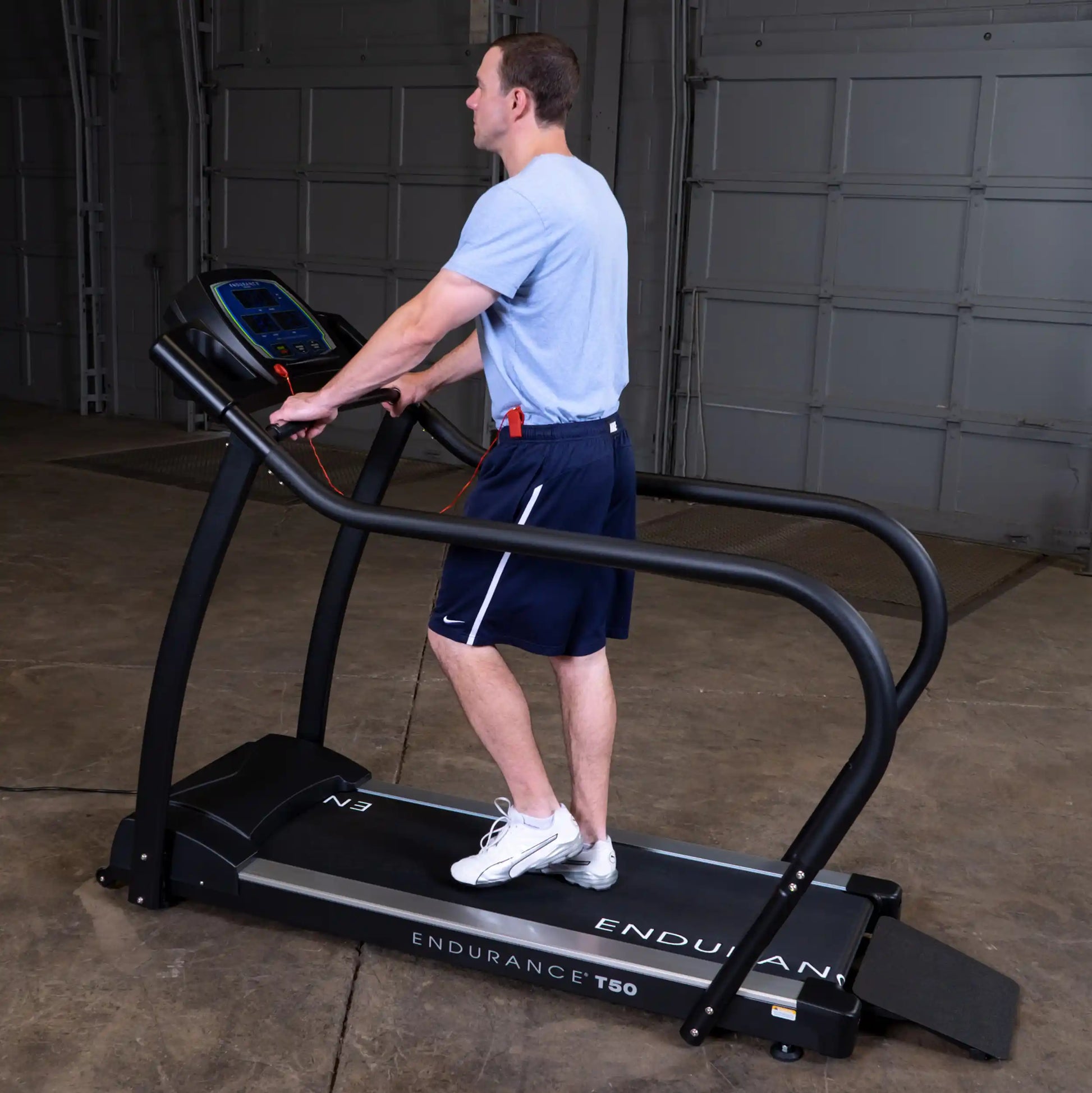 Man walking on Endurance T50 treadmill in a garage setting, wearing athletic shorts and white shoes.