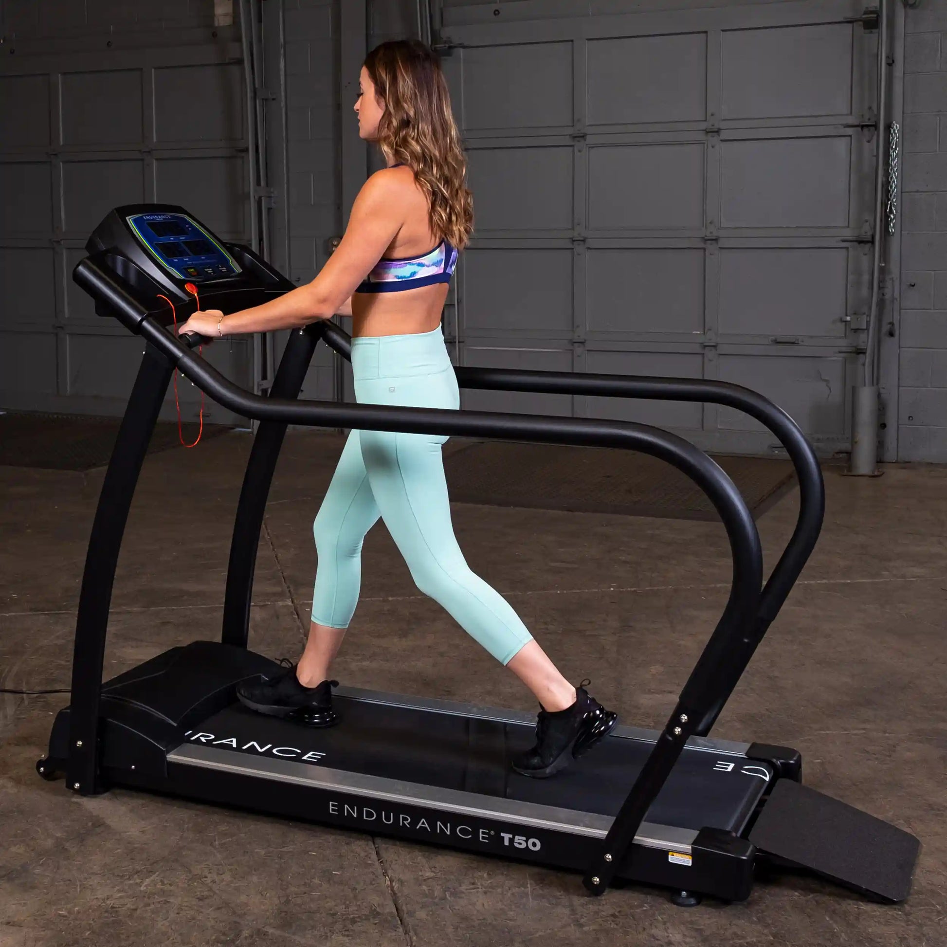 Woman walking on Endurance T50 treadmill in mint leggings, featuring curved design in a garage setting.
