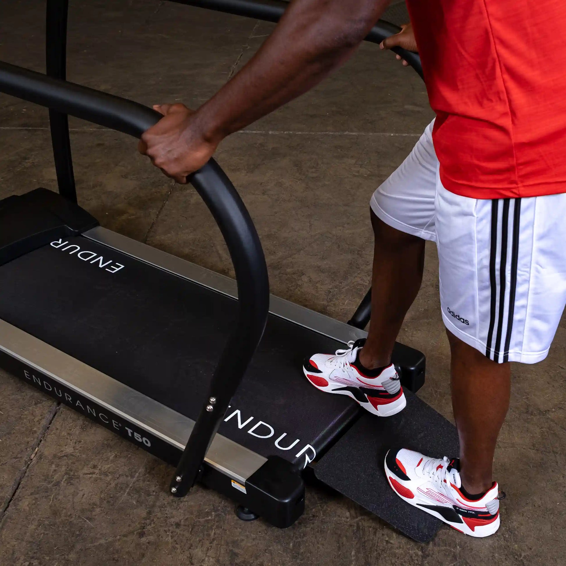 Man in Adidas shorts using Endurance T50 treadmill in a gym.