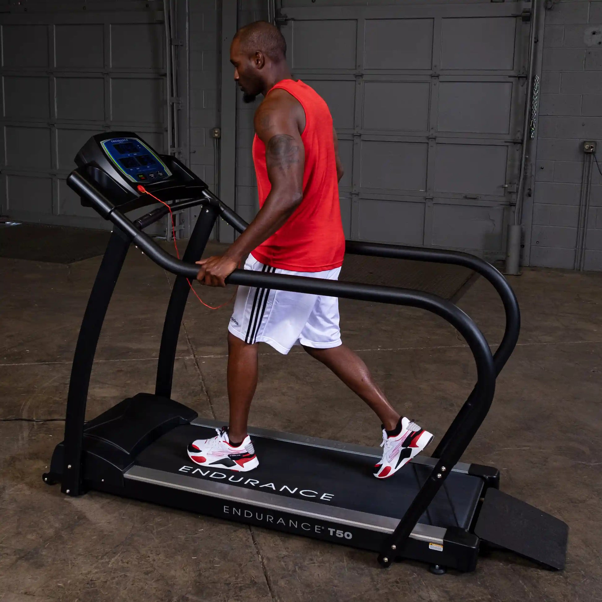 Man in red shirt using Endurance T50 treadmill in a garage setting.