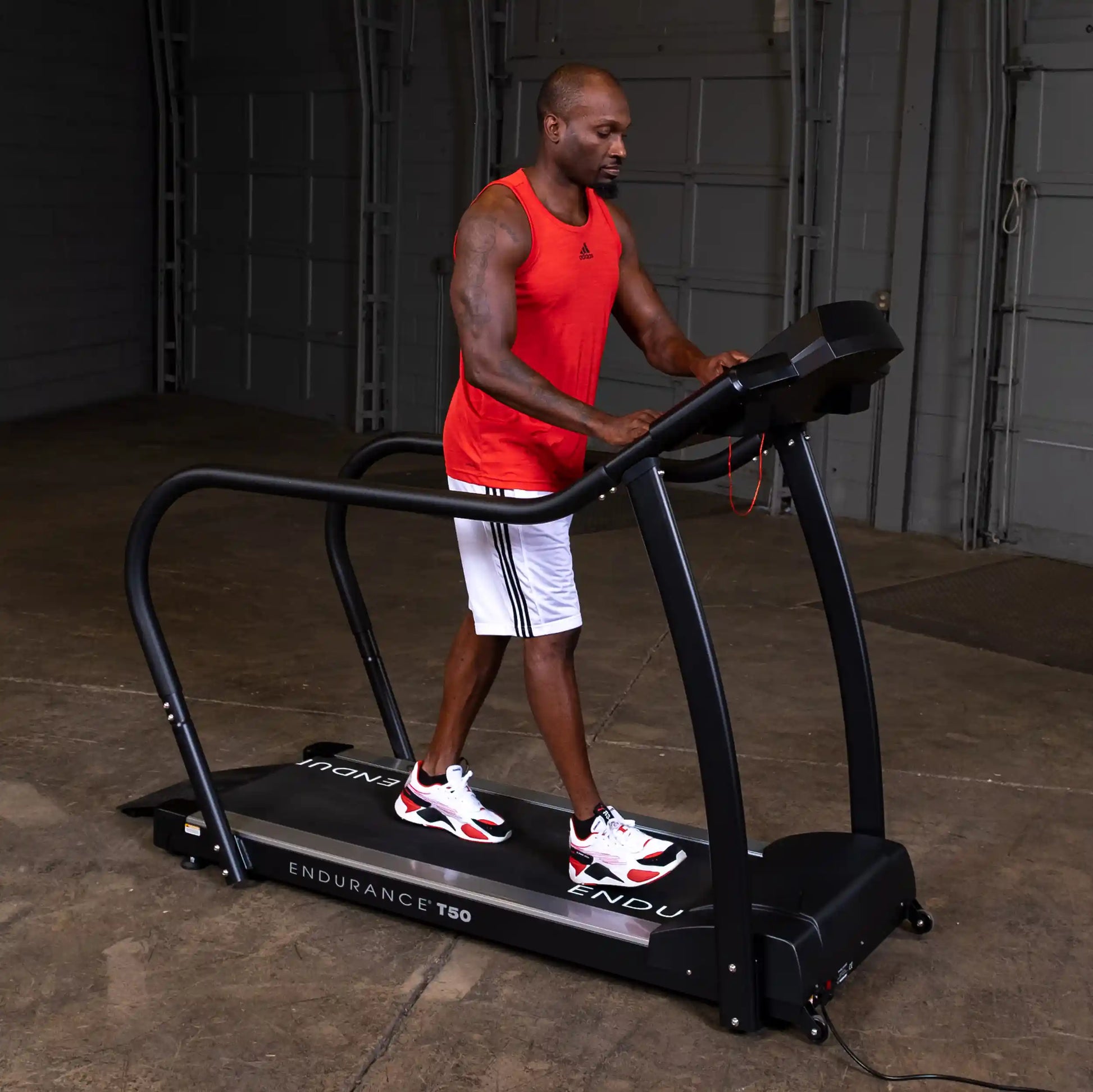 Man exercising on Endurance T50 treadmill in a garage, wearing red tank top and white shorts.