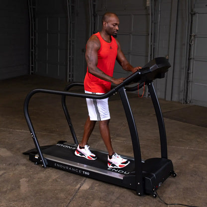 Man exercising on Endurance T50 treadmill in a garage, wearing red tank top and white shorts.