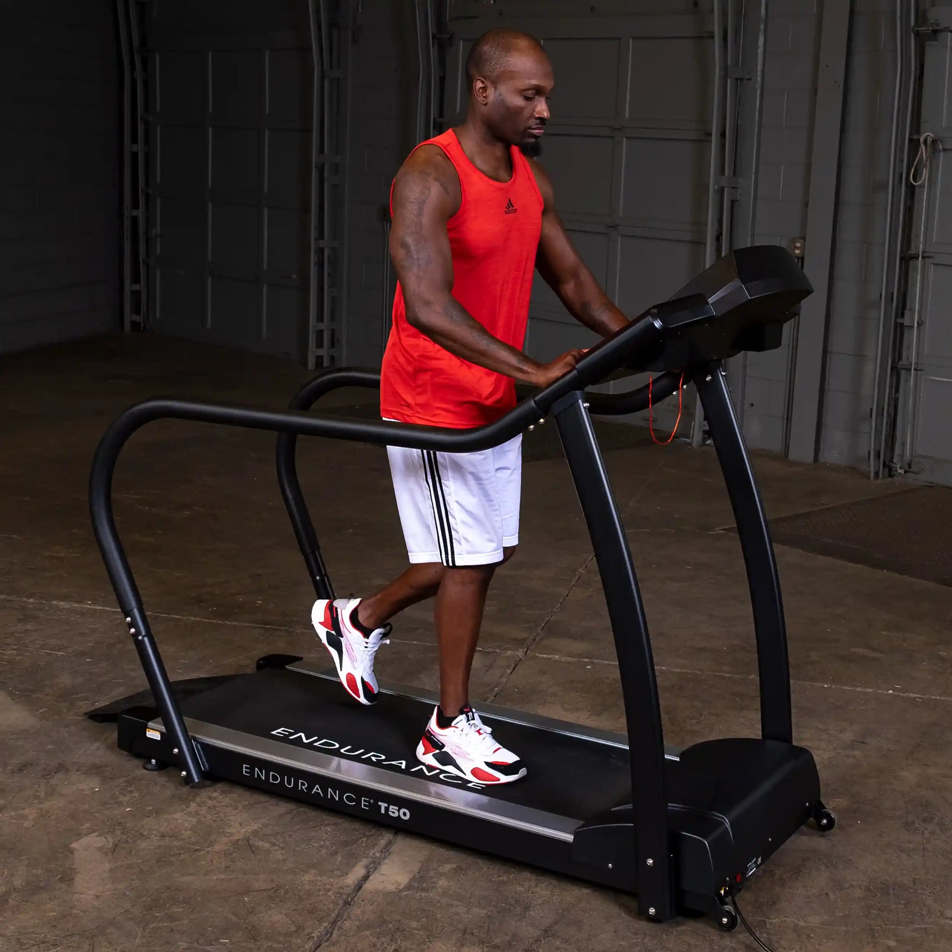 Man exercising on Endurance T50 treadmill in a red tank top in a garage setting.