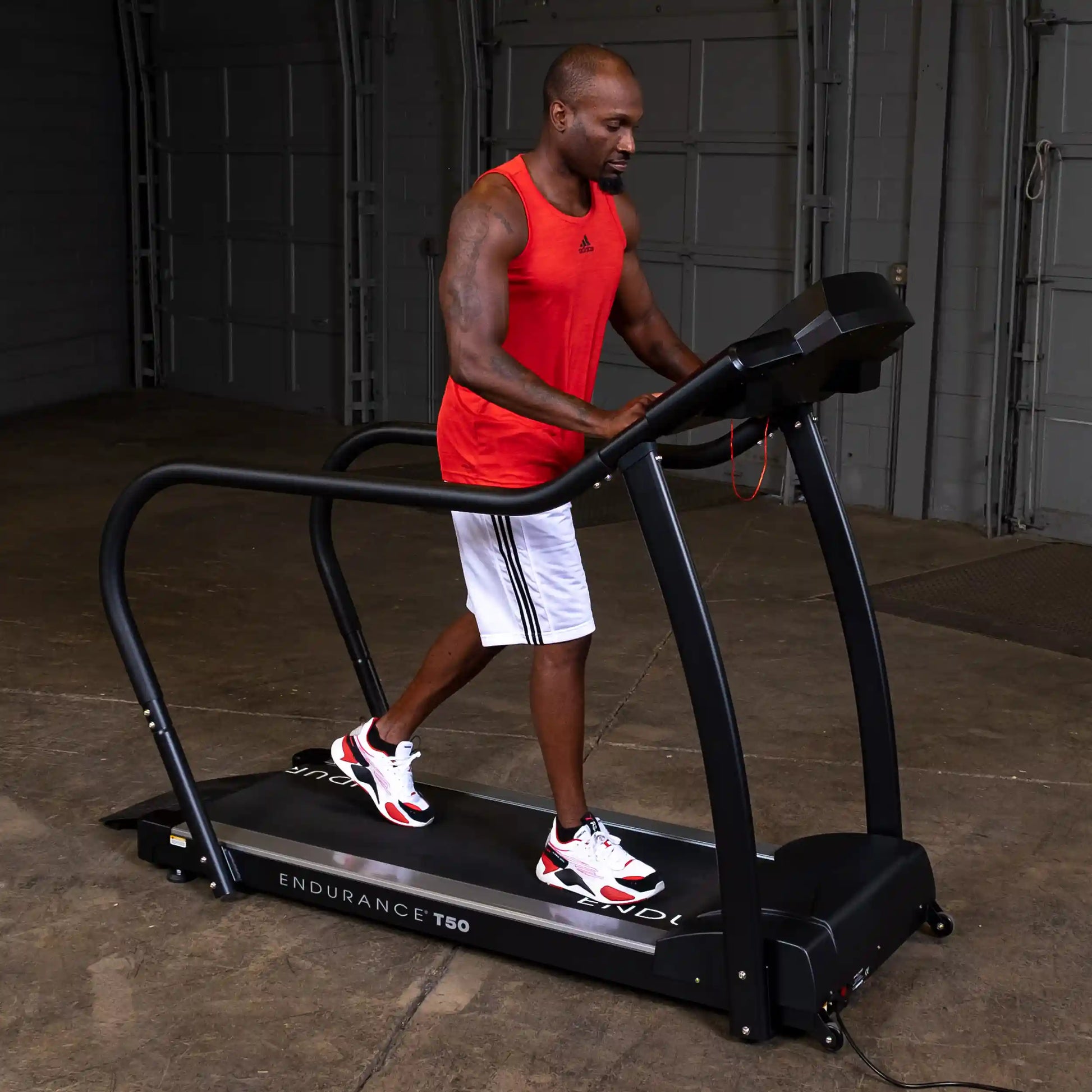 Man exercising on Endurance T50 treadmill in a garage gym wearing a red tank top and white shorts.