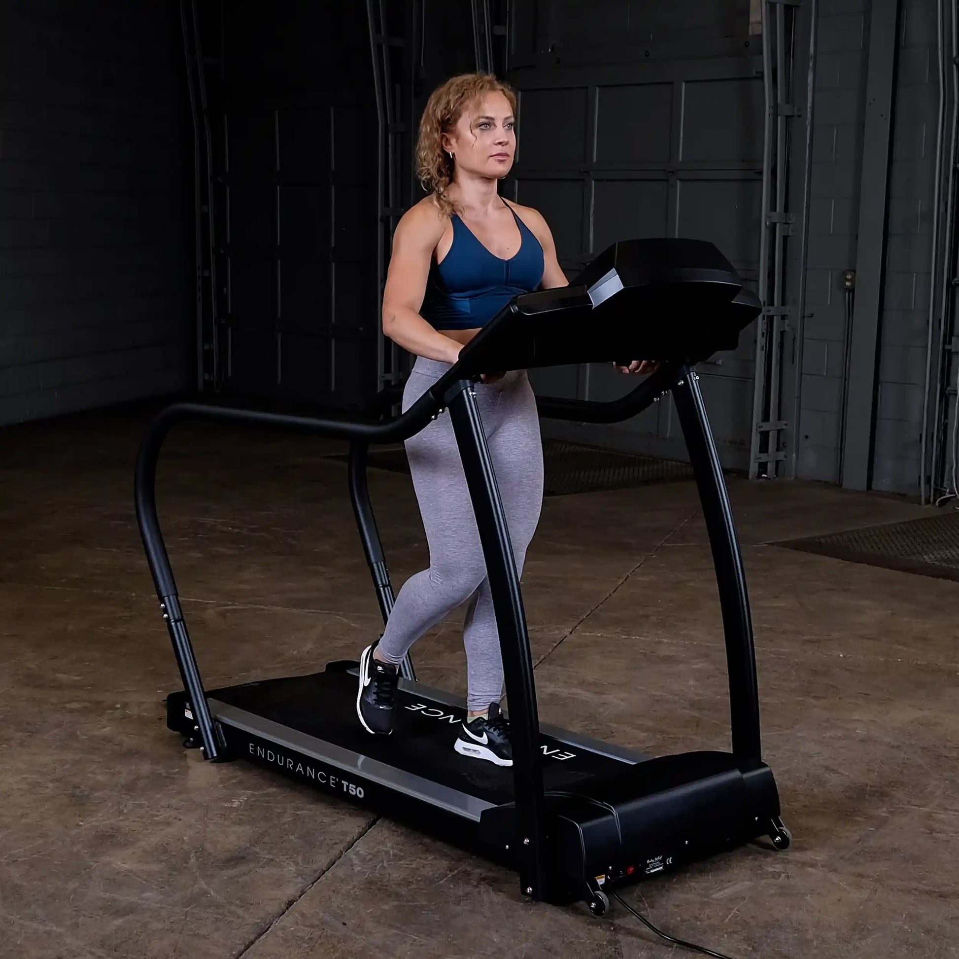 Woman walking on Endurance T50 treadmill in a dark gym.