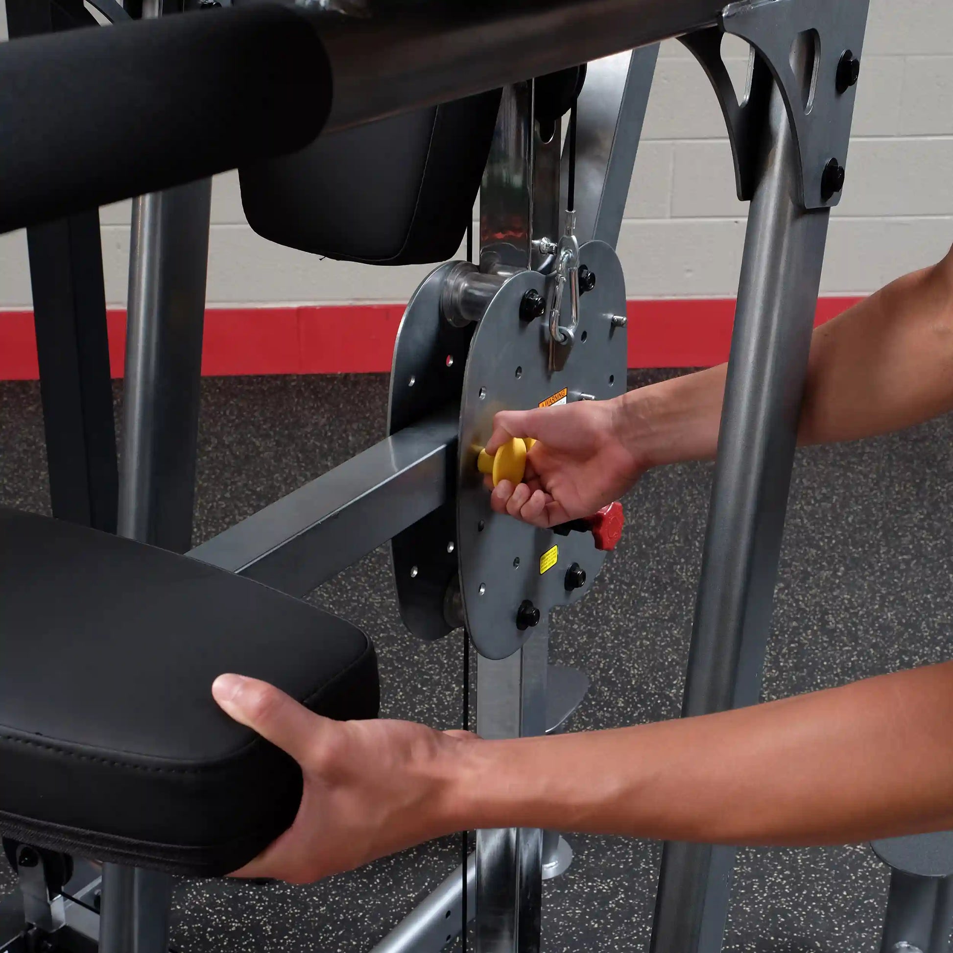 Adjusting weight on a black leg press machine with a yellow knob in a gym.