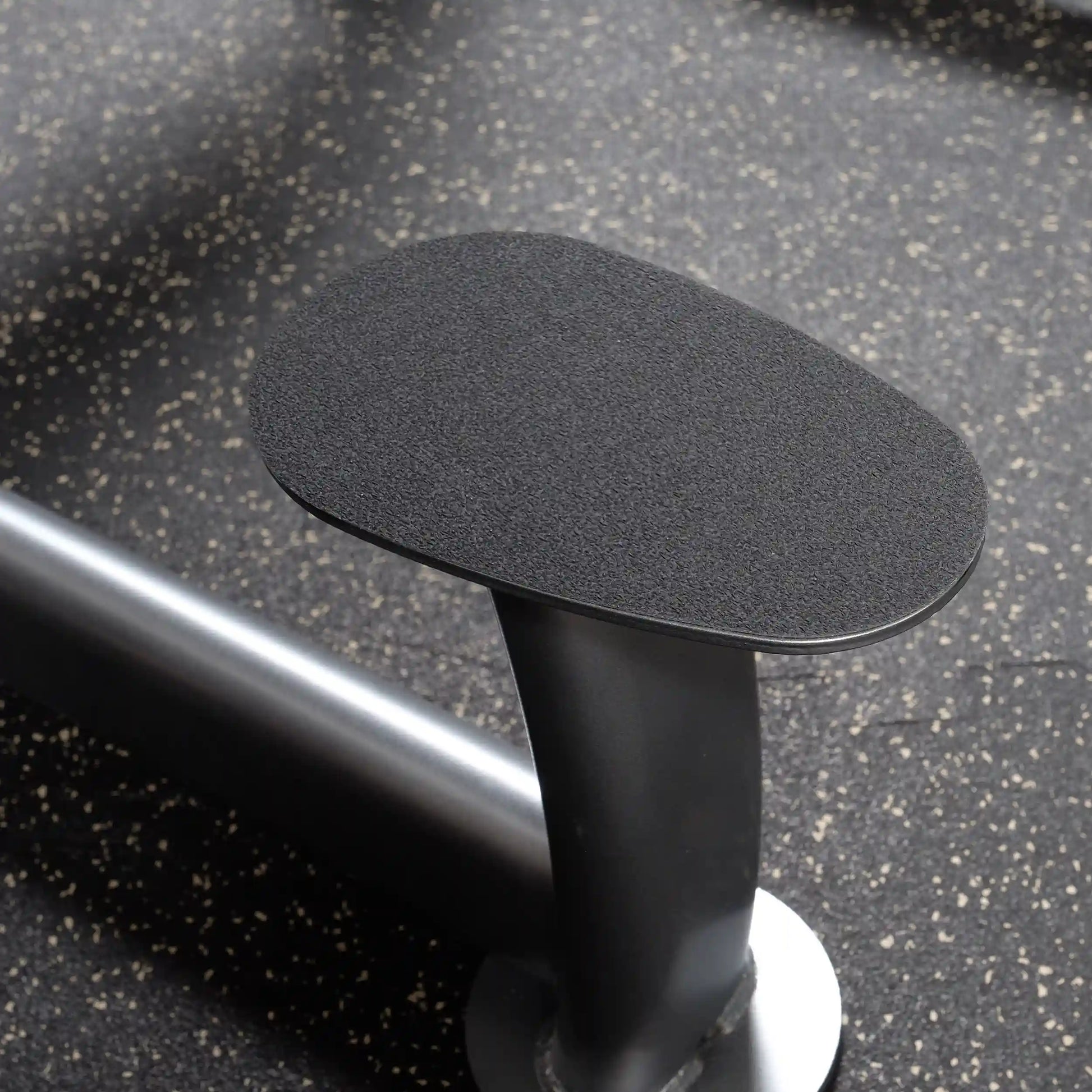 Gym arm blaster pad with black non-slip surface on speckled floor.