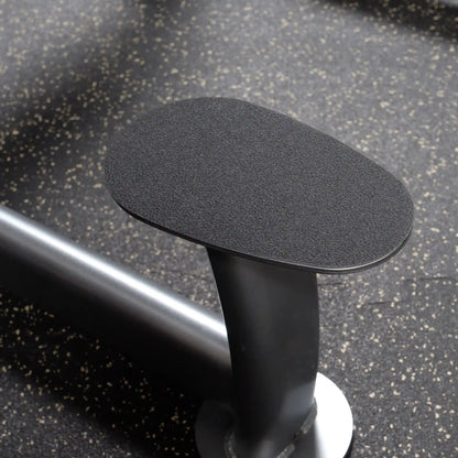 Gym arm blaster pad with black non-slip surface on speckled floor.