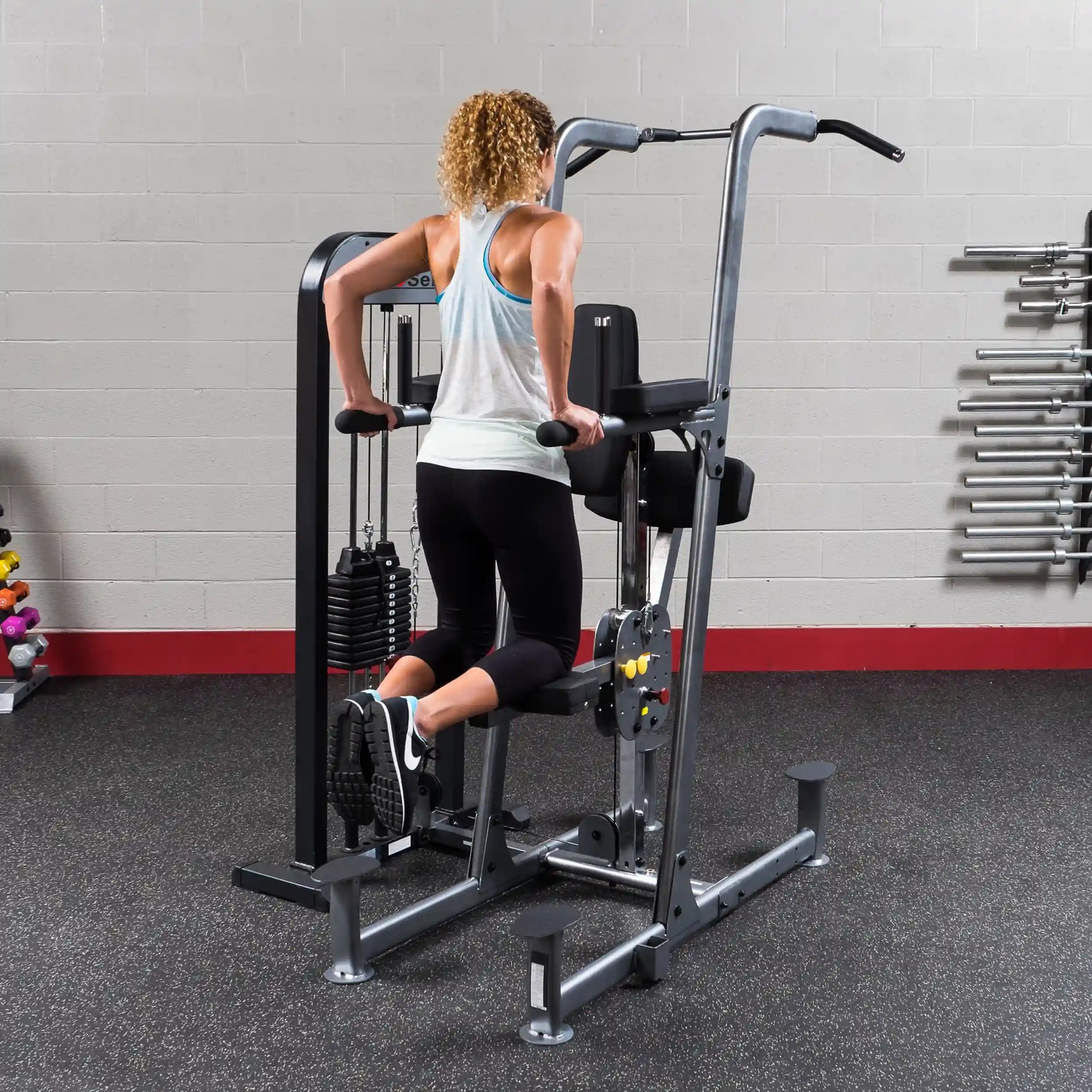 Woman using Body-Solid dip machine in gym, performing tricep exercise.
