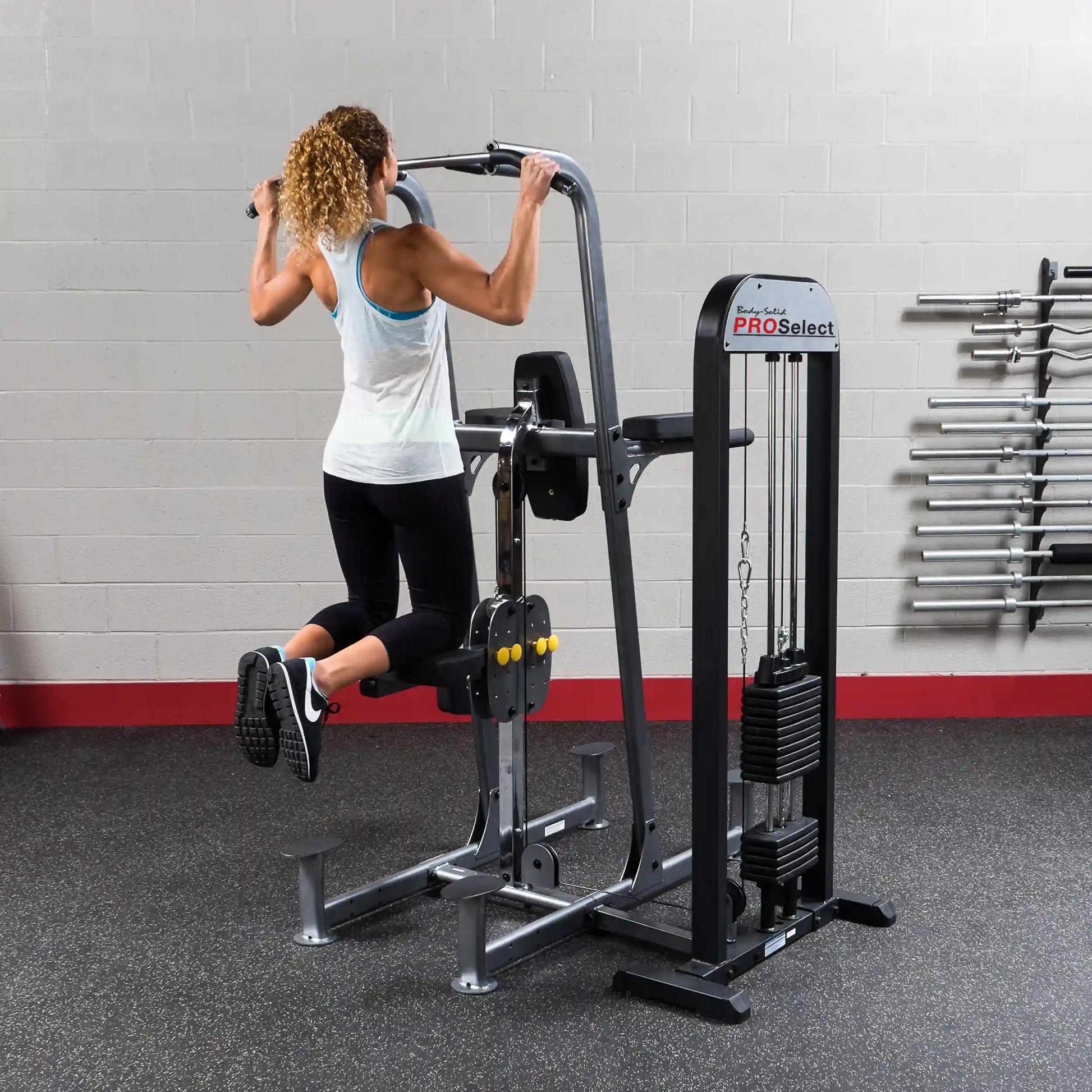 Woman using Body-Solid PRO Select pull-up machine with weight assist in gym.