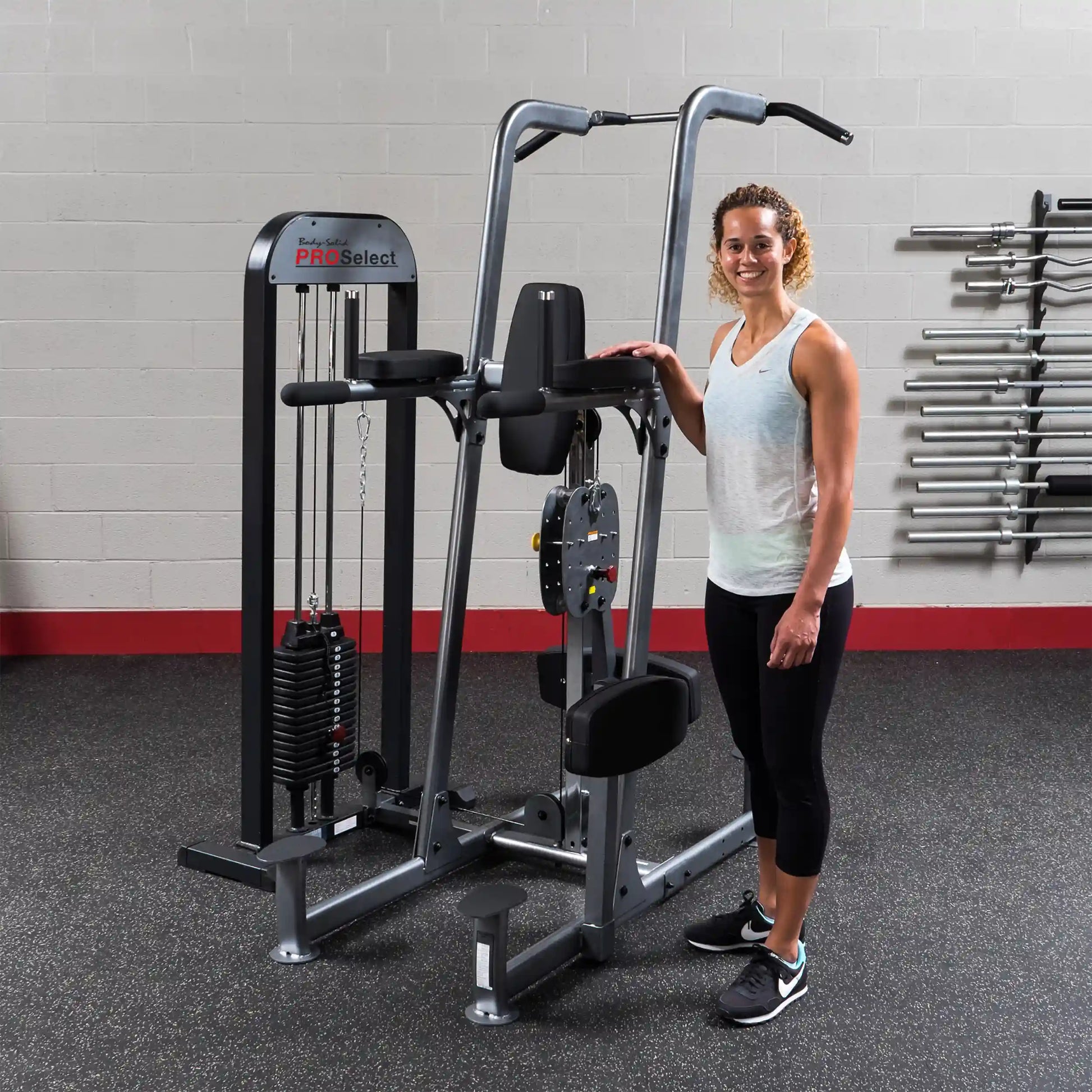 Woman standing beside Body-Solid ProSelect weight machine in gym.