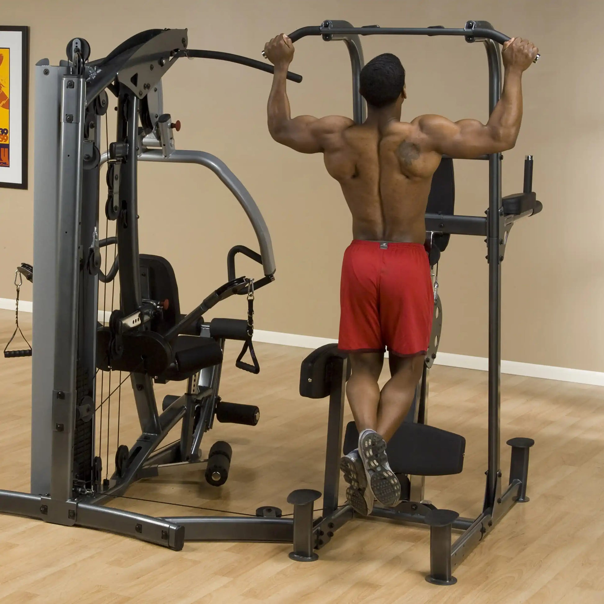 Man doing pull-ups on home gym machine in red shorts.