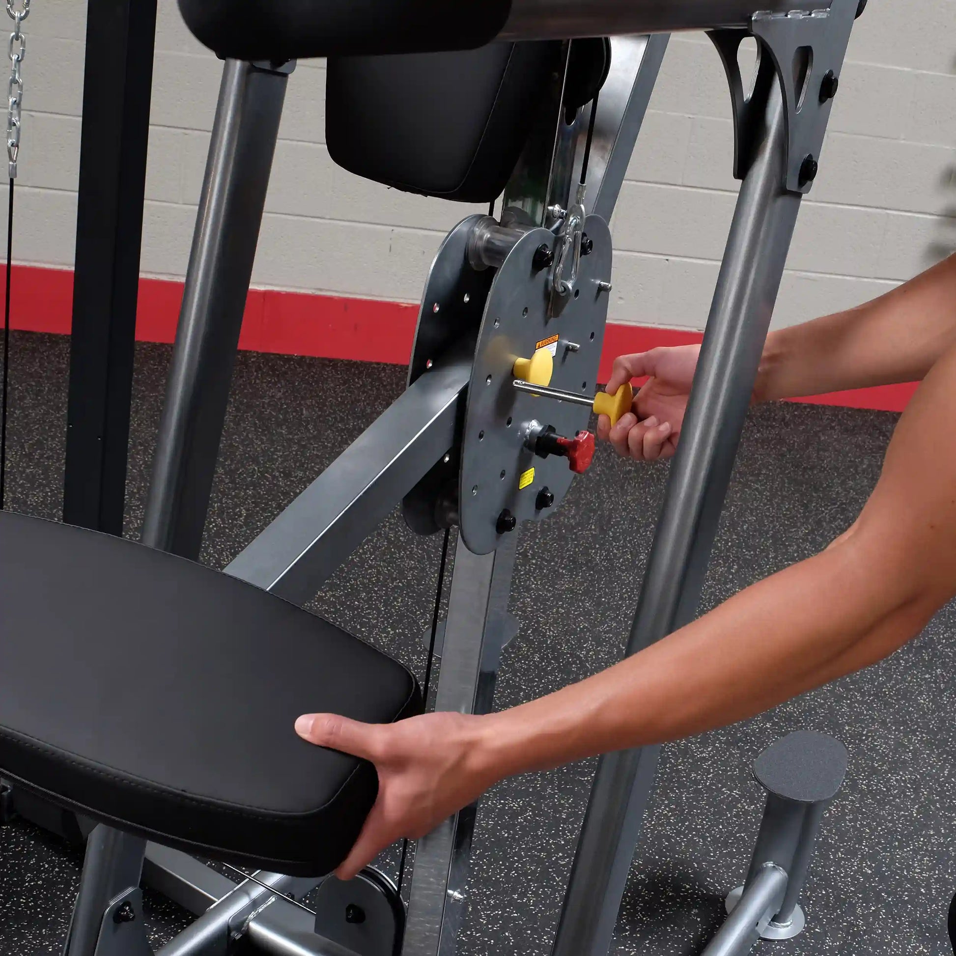 Person adjusting a weight machine lever in a gym setting.