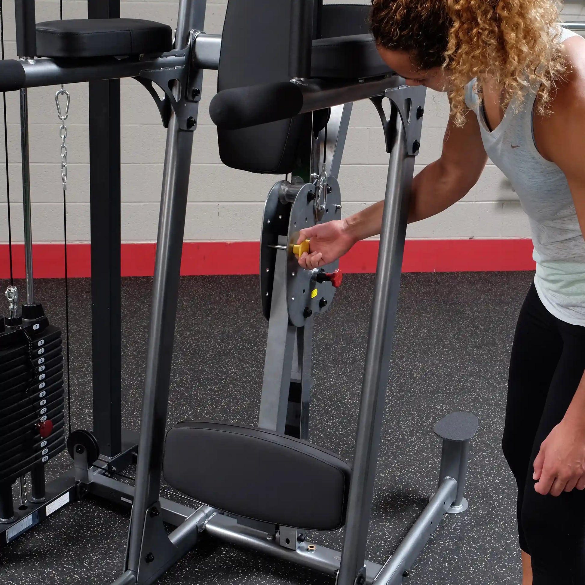 Woman adjusting a weight machine in a gym, demonstrating equipment use.