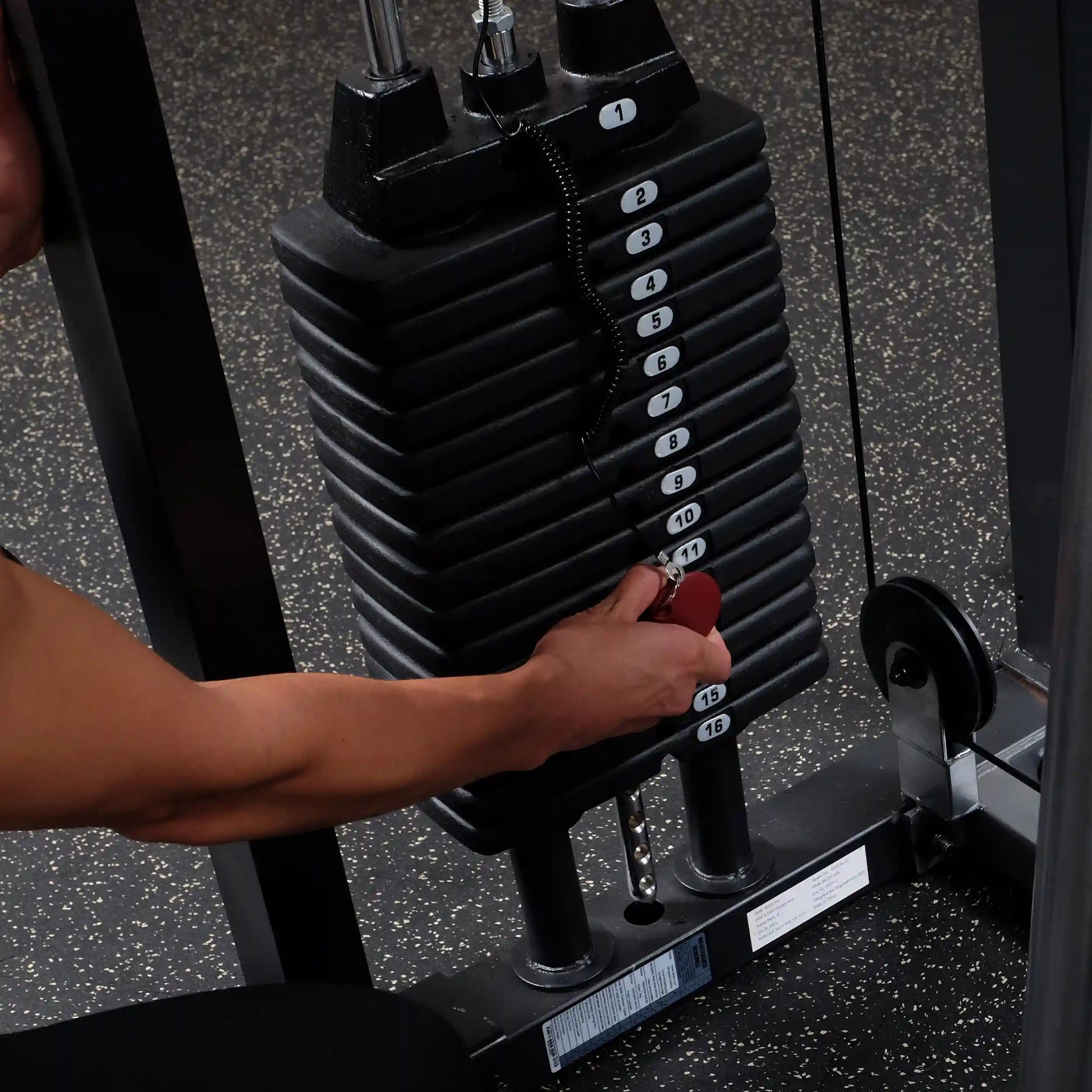 Adjusting weight stack on gym machine with numbered plates and red pin.