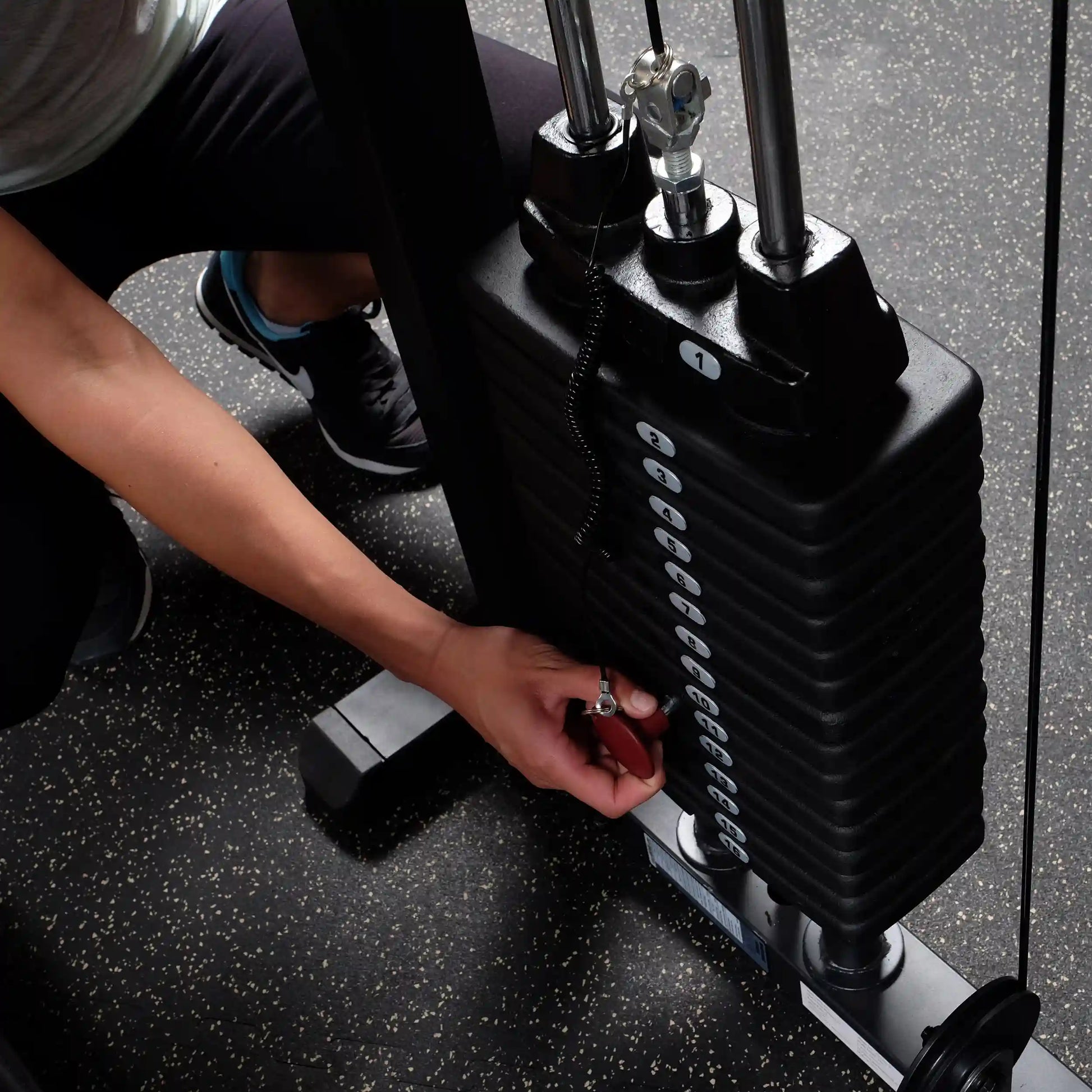 Adjusting weight stack on gym equipment with pin for strength training.