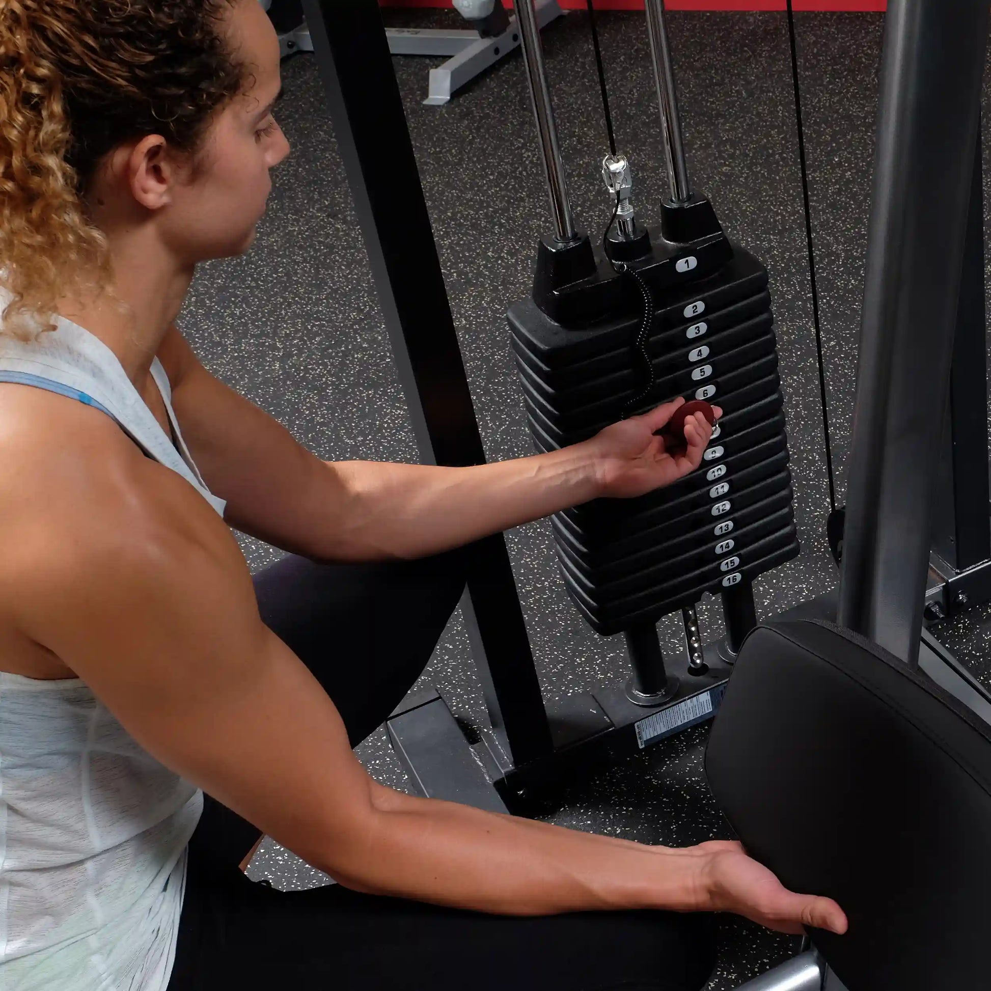 Woman adjusting a weight stack on a cable machine in a gym.