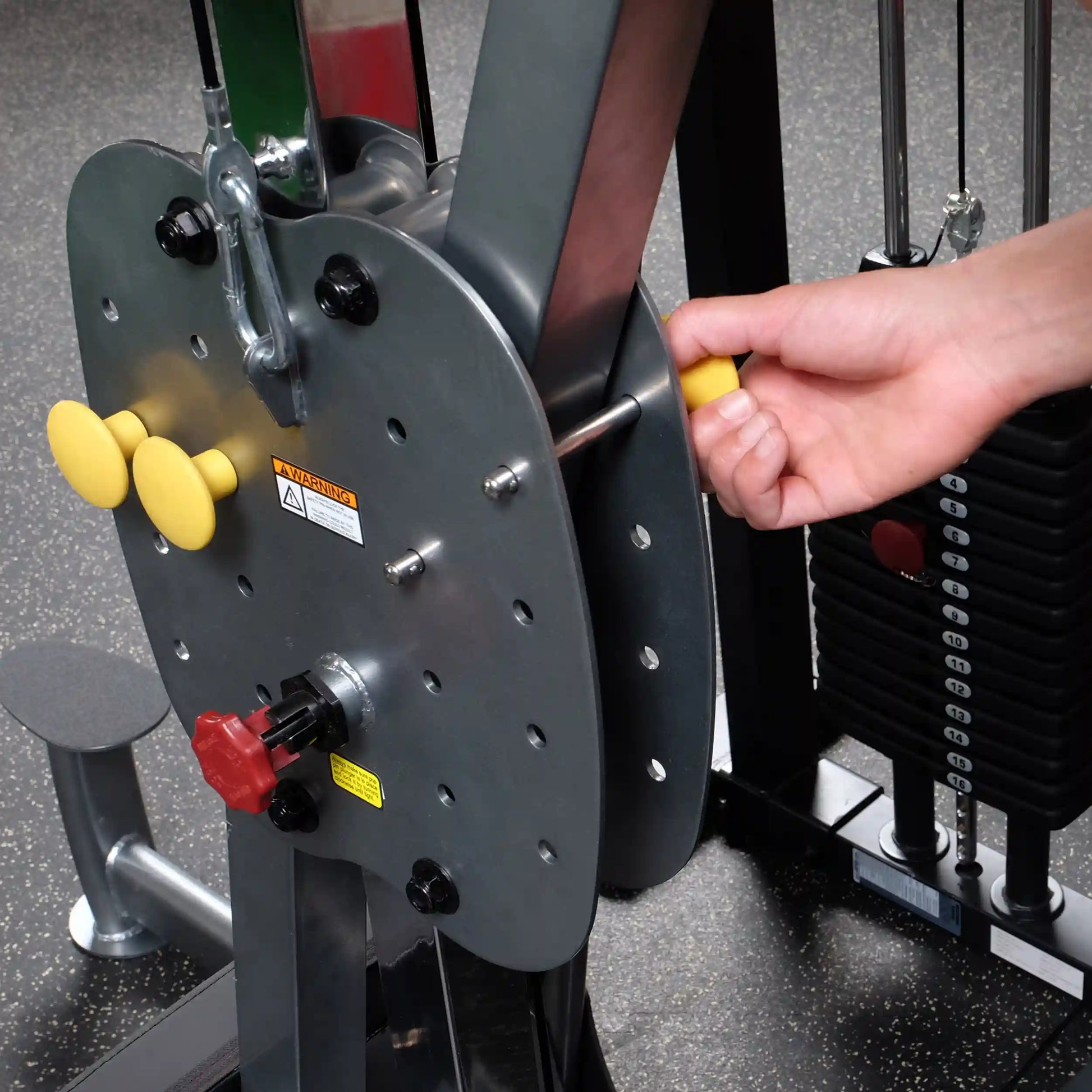 Adjusting weight on gym machine with yellow handle, black weight stack visible.